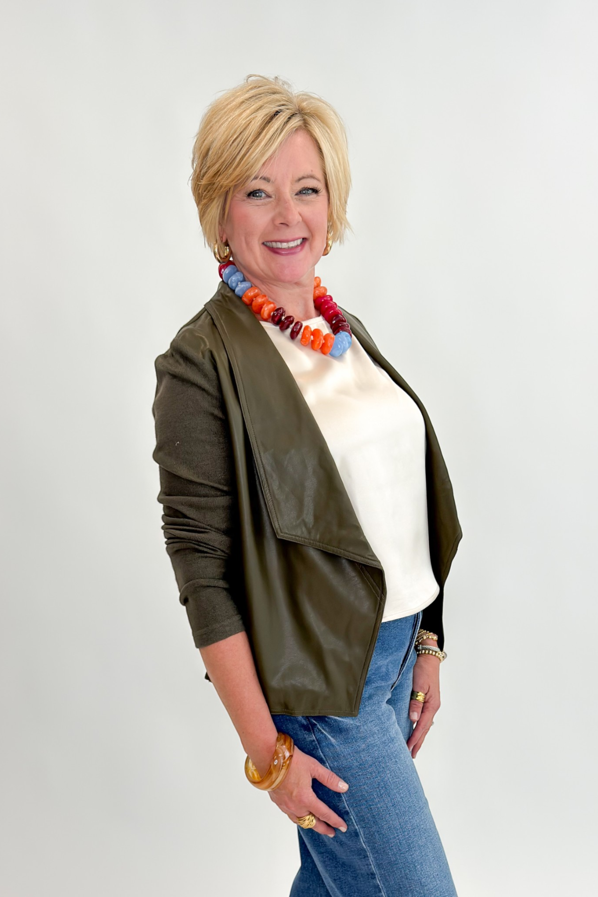 Side view of woman wearing Swagger Boutique’s Olive Knit & Faux Leather Draped Jacket with Maya Wide Leg Jeans In Medium Wash- Journey by Kut from the Kloth against white studio background.