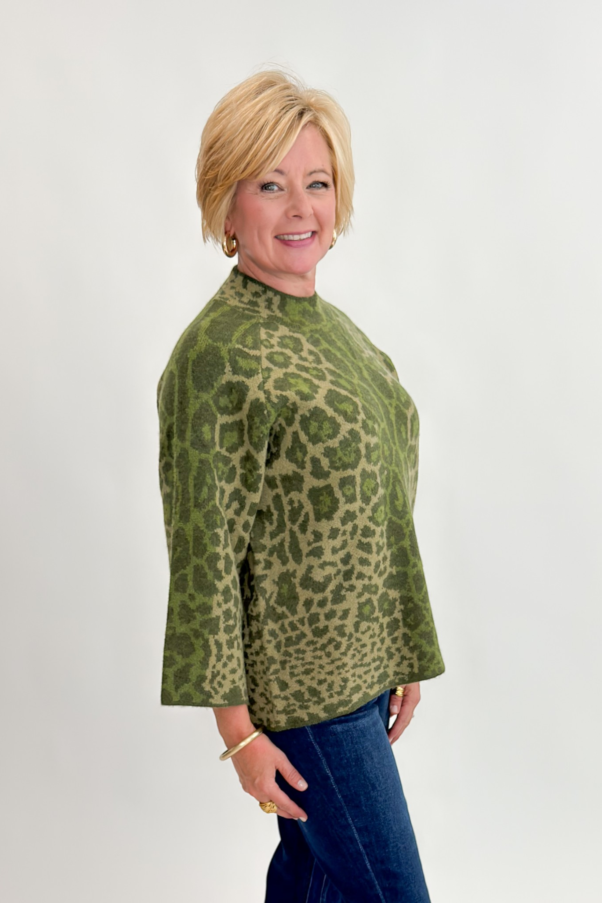 Side view of woman wearing Swagger Boutique’s Olive Leopard Print Mock Neck Sweater by Entro with jeans against white studio background.