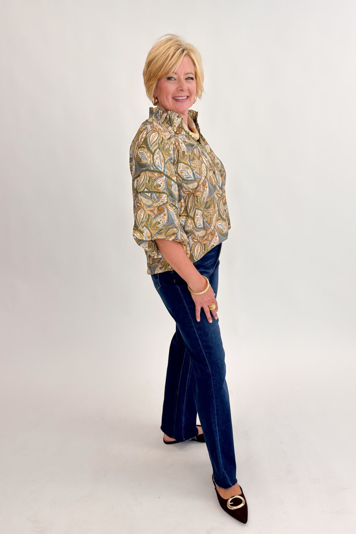 Side view of woman wearing Swagger Boutique’s Olive Printed 3/4 Sleeve Top with jeans against white studio background.