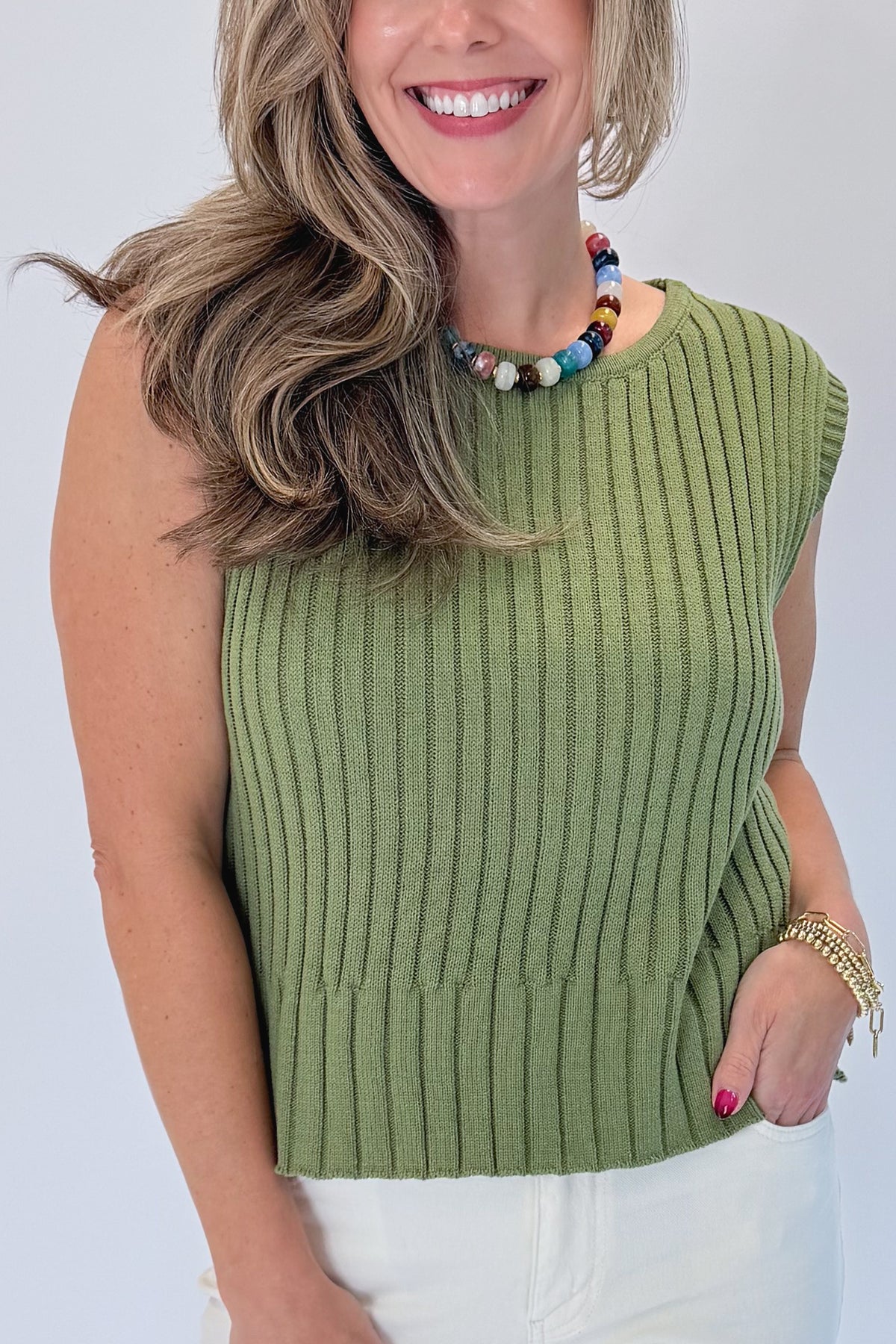 Front detail view of woman wearing Swagger Boutique’s Olive Ribbed Sleeveless Sweater with jeans against white studio background.