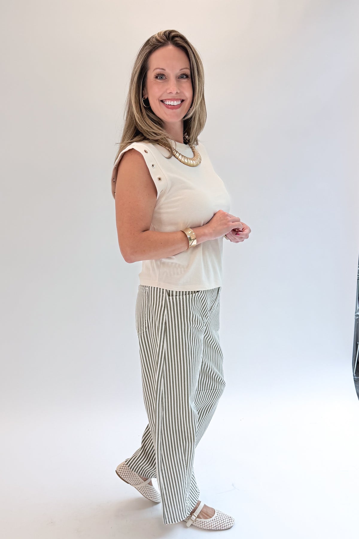 Side view of woman wearing Swagger Boutique’s top with Olive Striped Barrel Jeans by Just Black Denim against white studio background.