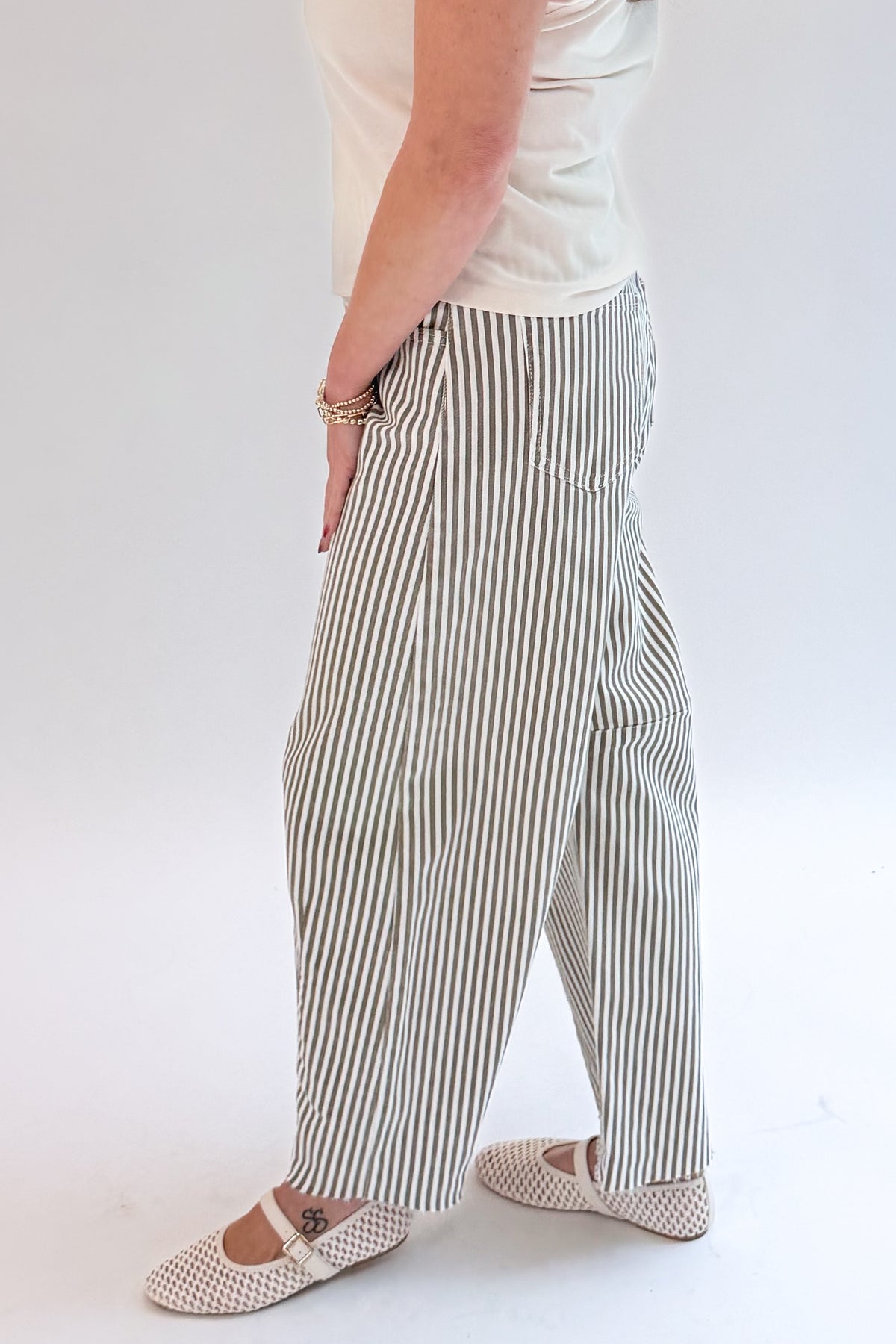 Side view of woman wearing Swagger Boutique’s top with Olive Striped Barrel Jeans by Just Black Denim against white studio background.