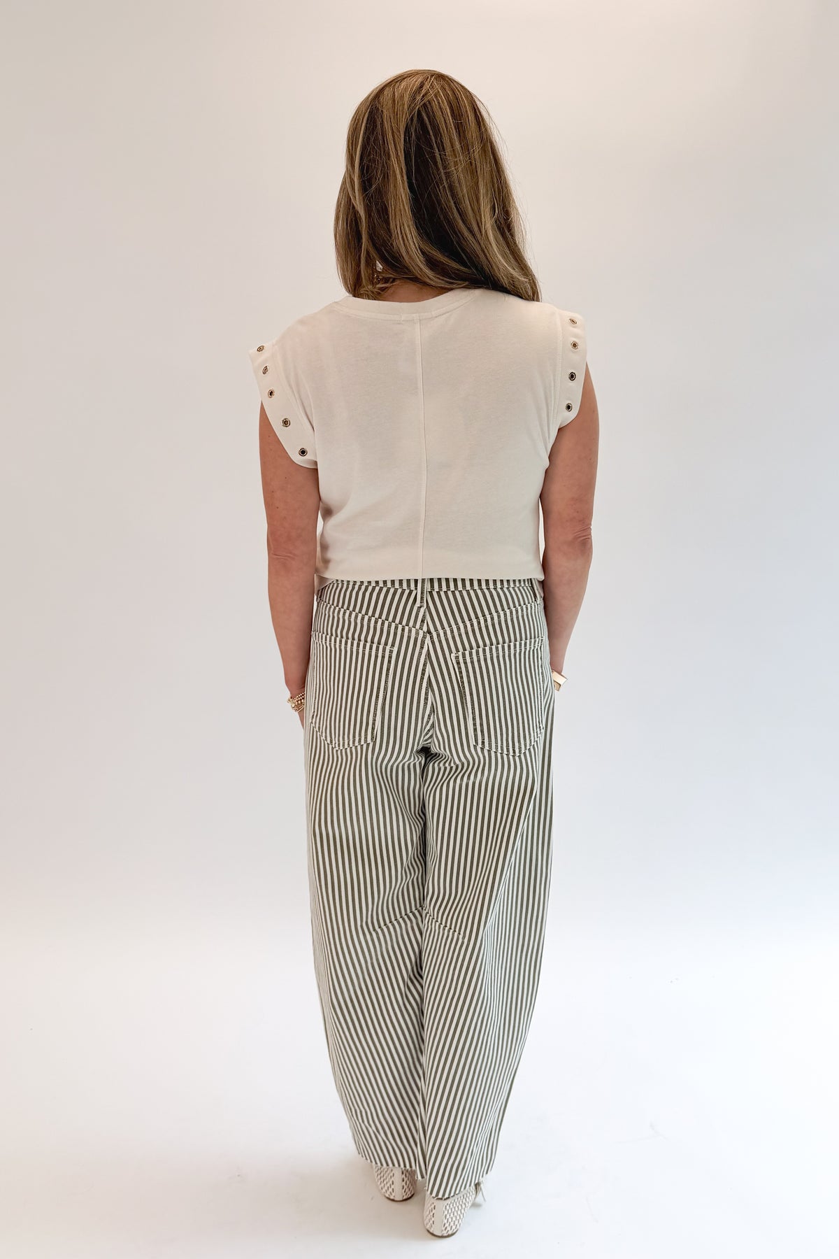 Back view of woman wearing Swagger Boutique’s top with Olive Striped Barrel Jeans by Just Black Denim against white studio background.