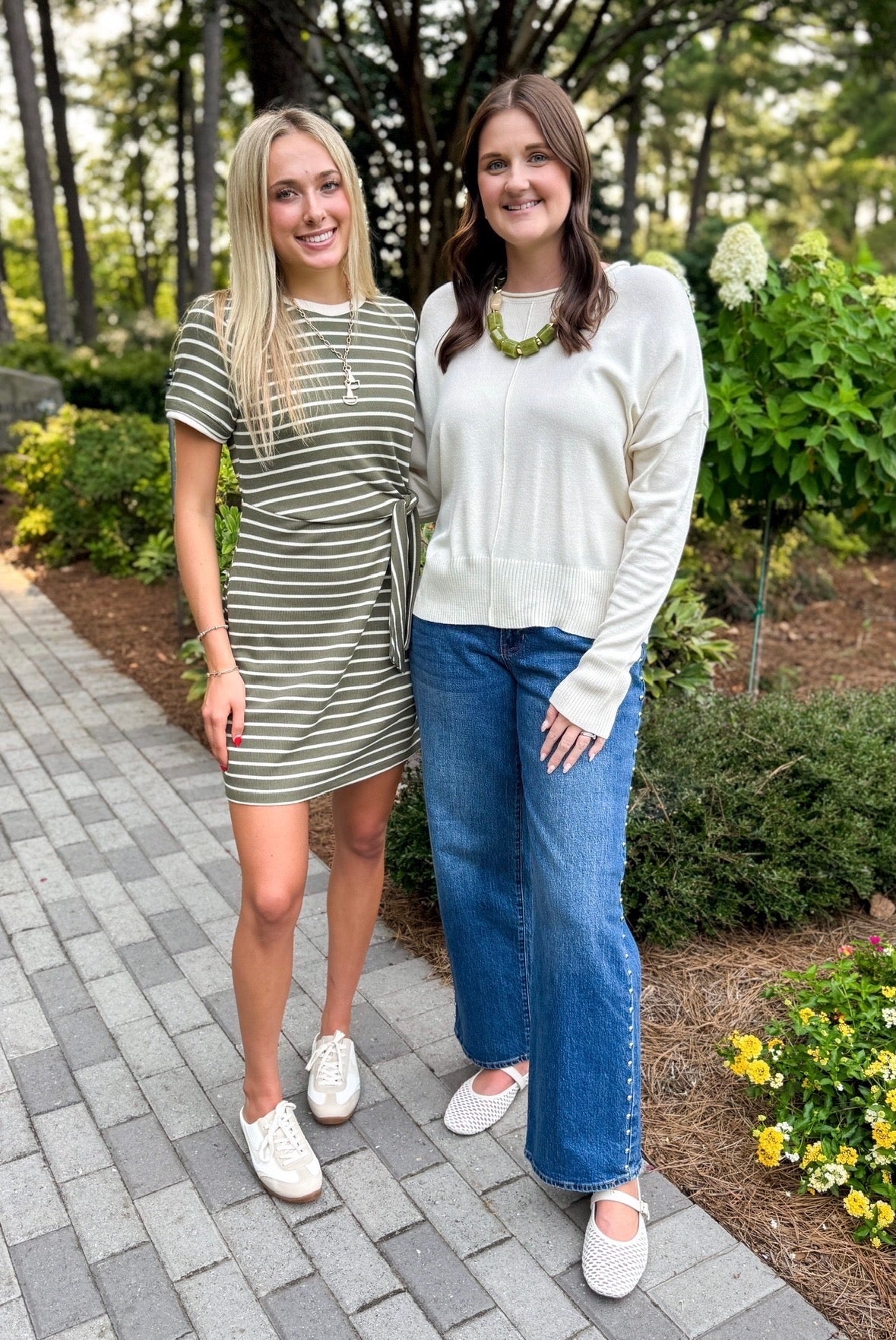 Front view of women wearing Swagger Boutique’s Olive Striped Tie Waist Mini Dress by Entro with sneakers and Cream Center Seam Round Neck Sweater standing outside on a pathway.