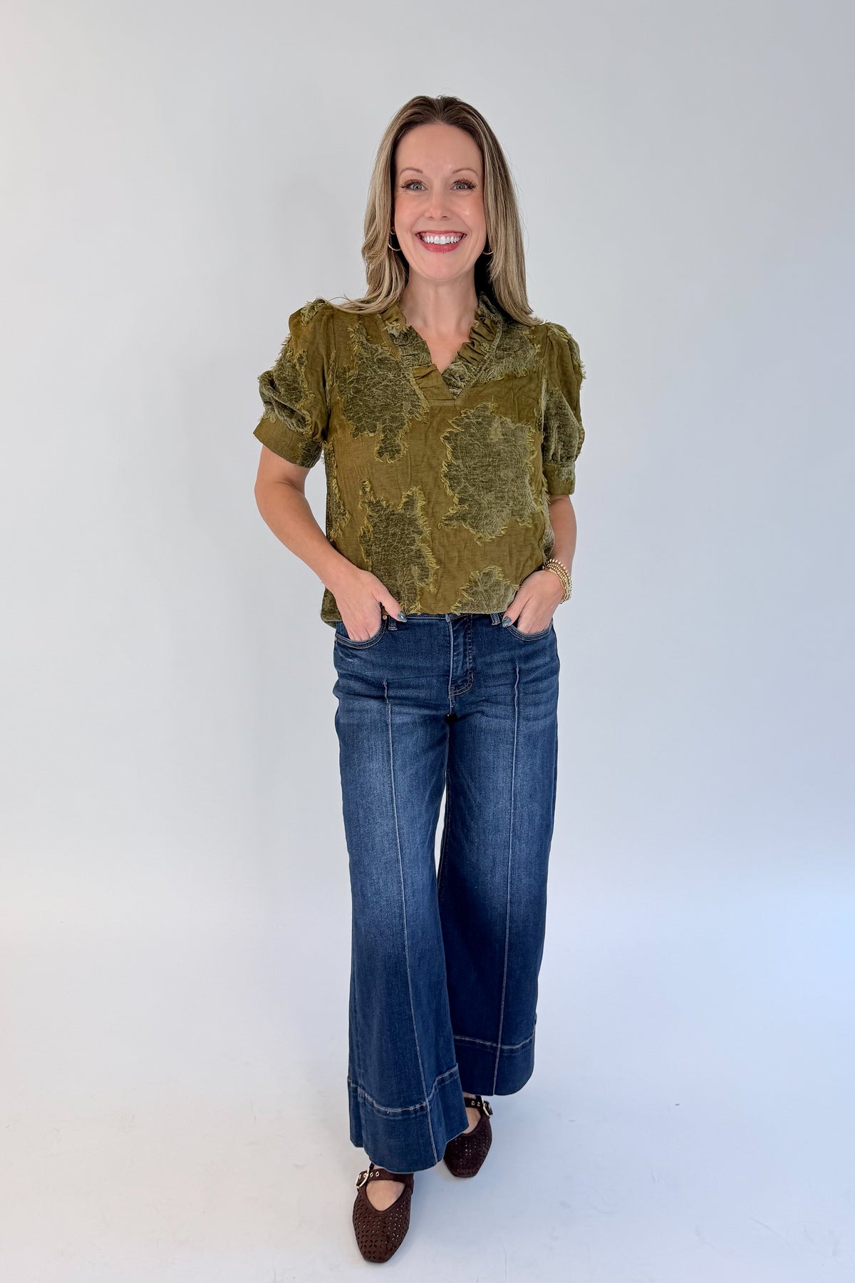 Front view of woman wearing Swagger Boutique’s Olive Velvet Ruffle Neck Top with jeans against white studio background.