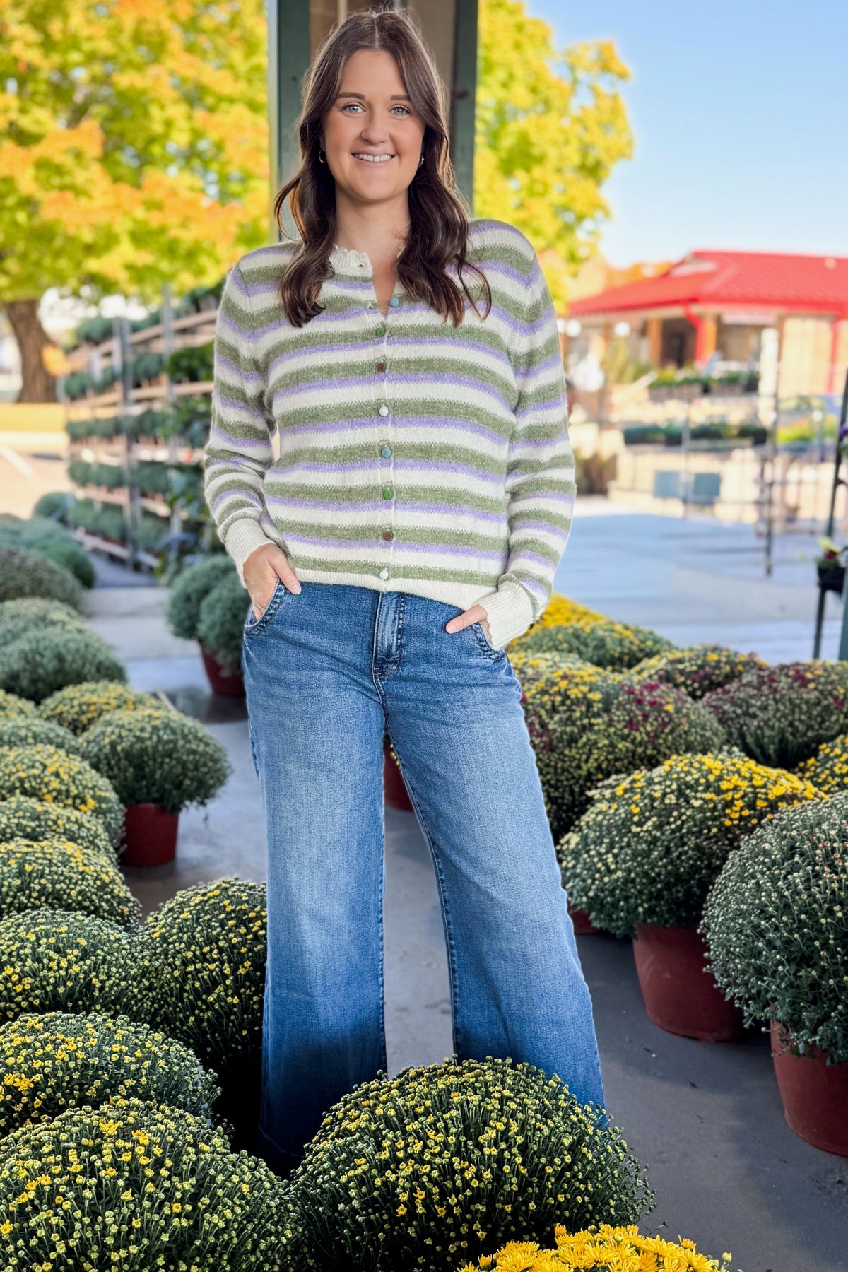 Front view of woman wearing Swagger Boutique’s Olive & Lavender Striped Button Up Cardigan with jeans at a garden center.