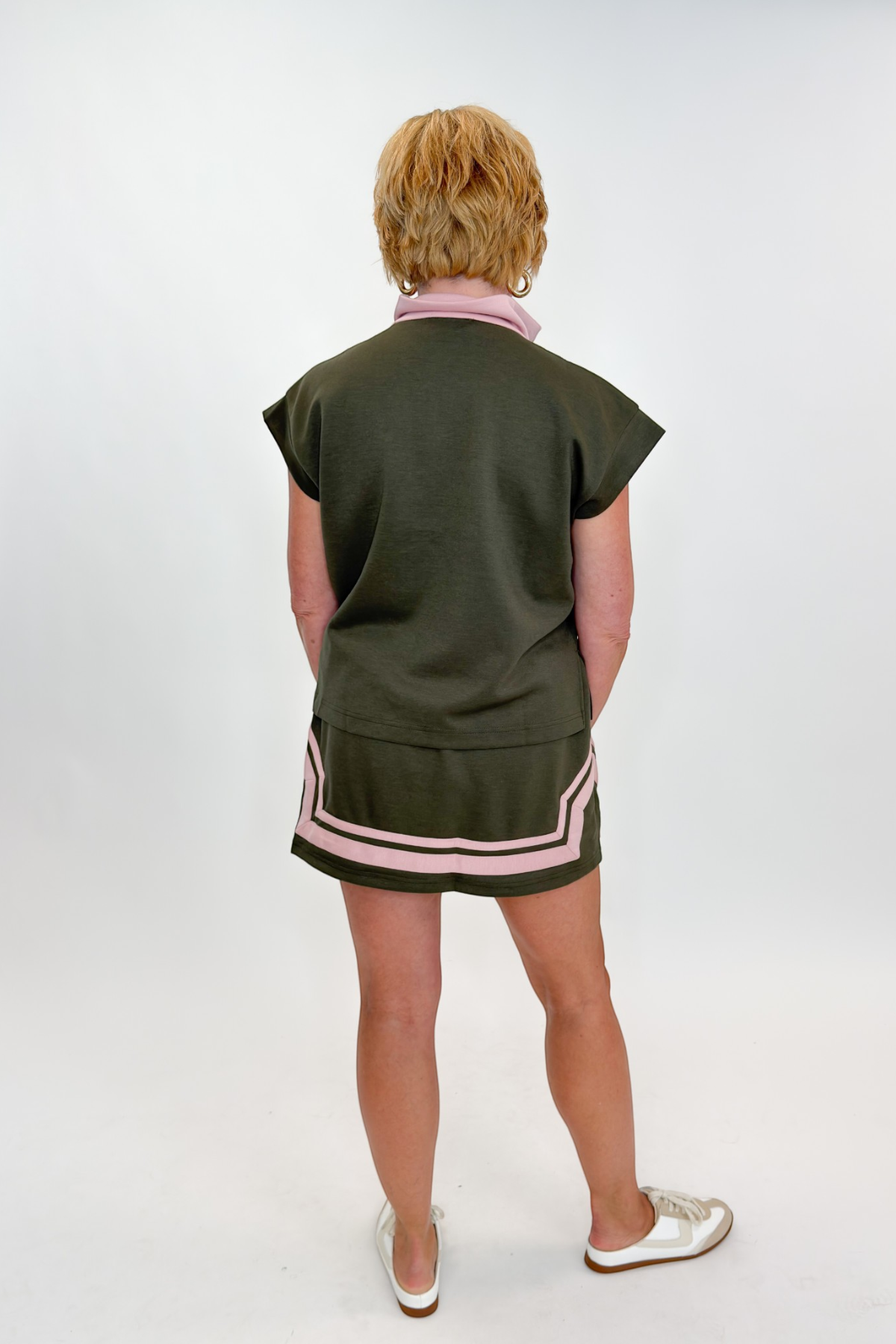 Back view of woman wearing Swagger Boutique’s Olive & Pink Half Zip Top & Skirt by Entro against white studio background.