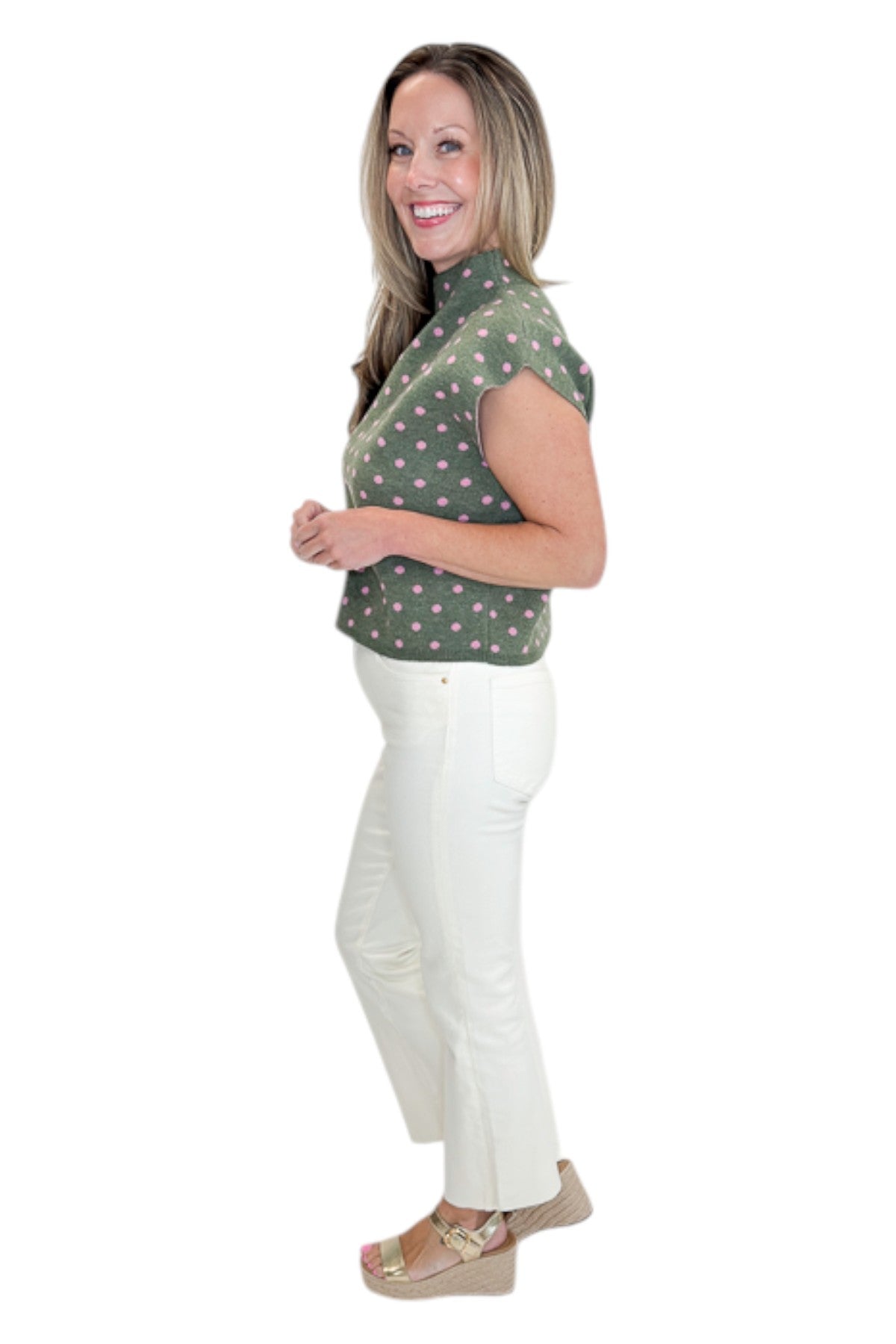 Side view of woman wearing Swagger Boutiqueās Olive & Pink Polka Dot Sleeveless Sweater by Entro with jeans against white studio background.