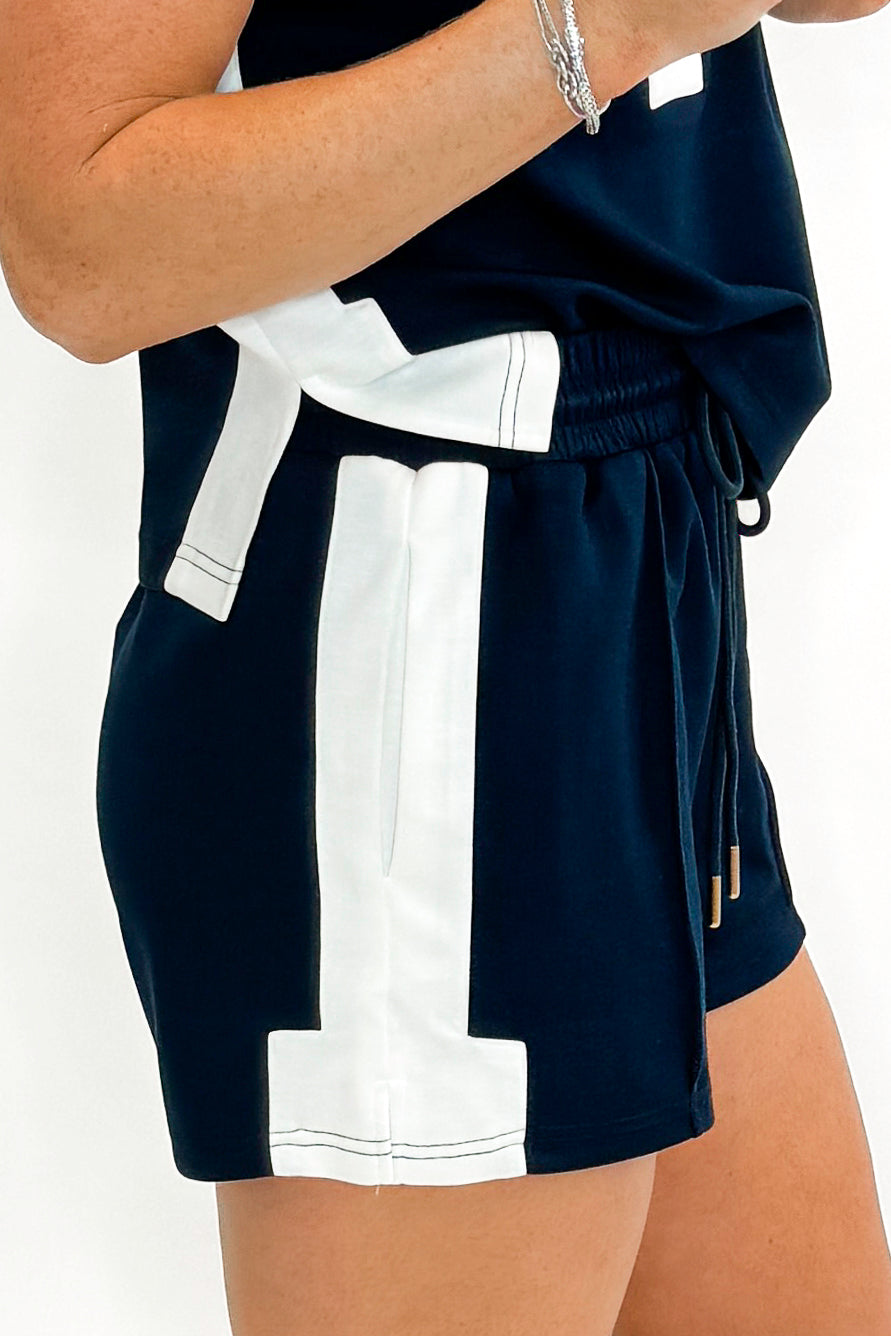 Side detail view of woman wearing Navy With White Color Block 1/4 Zip Sweatshirt by Entro with matching Navy With White Color Block Stripe Shorts by Entro against white studio background.