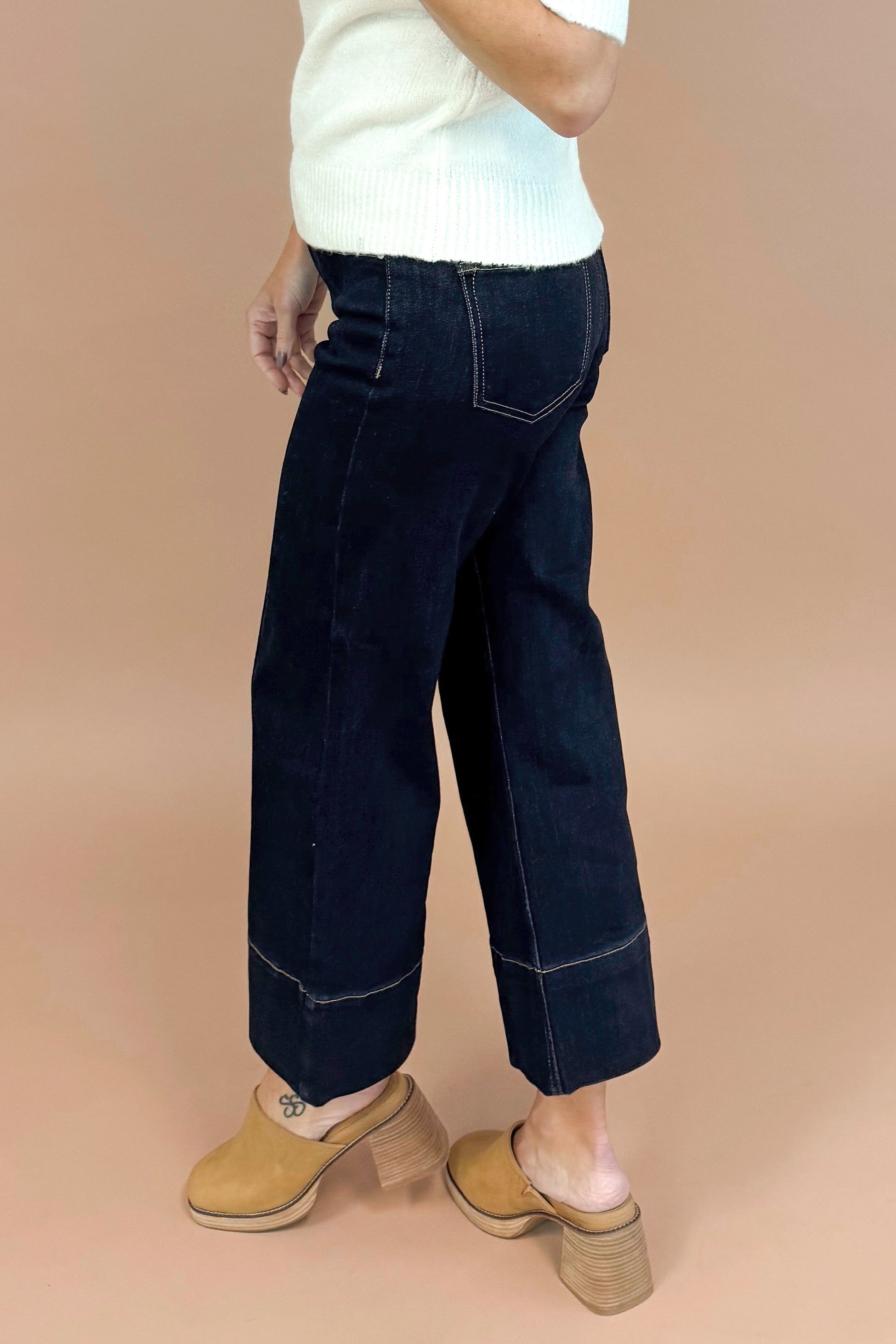Person wearing dark blue pants and a white top on a beige background