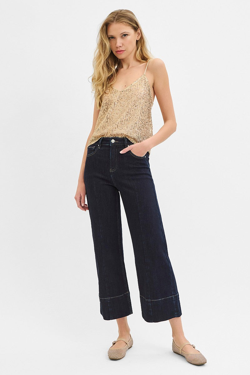 Woman wearing a gold sequin top and dark blue jeans on a white background
