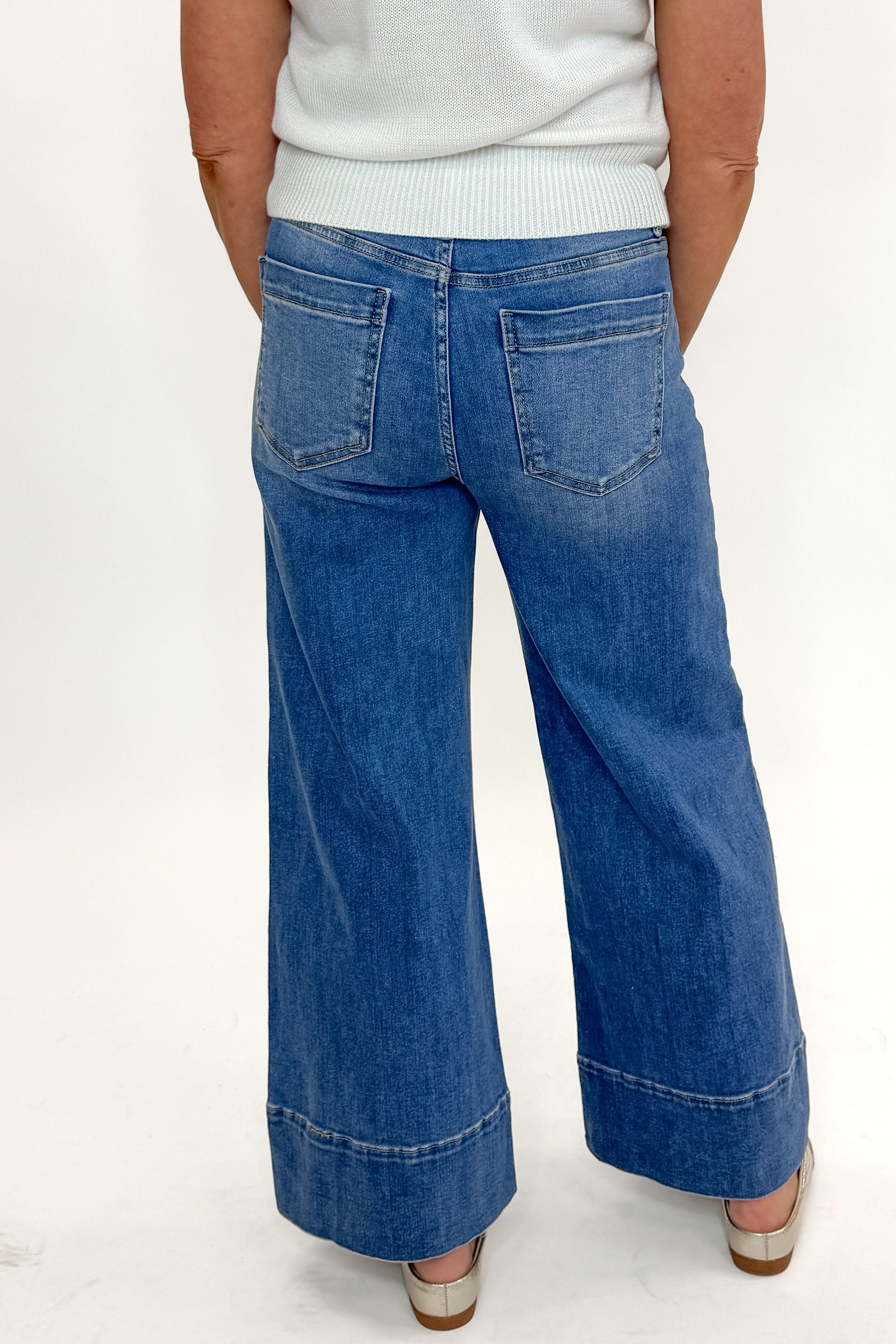 Back view of woman wearing Medium Wash Pintuck Detail Jeans by Risen with white sweater against white studio background.
