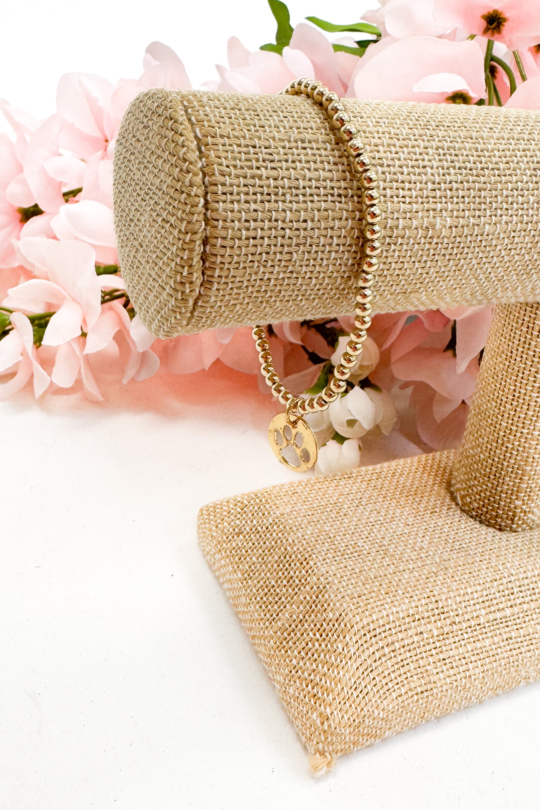 Gold bracelet on a decorative stand with pink flowers in the background
