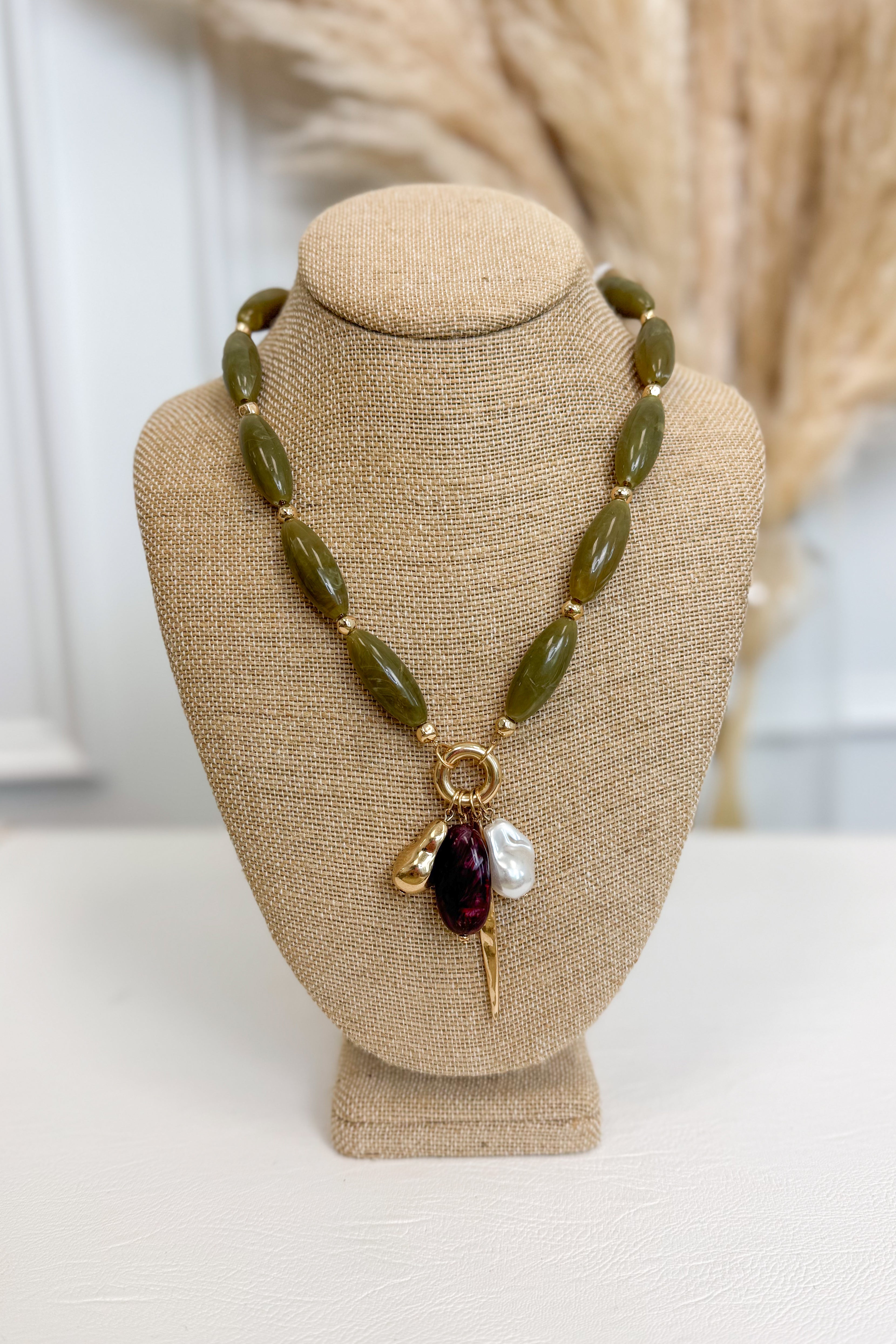 front view of olive necklace with pearl, plum, and gold accent charms on bust