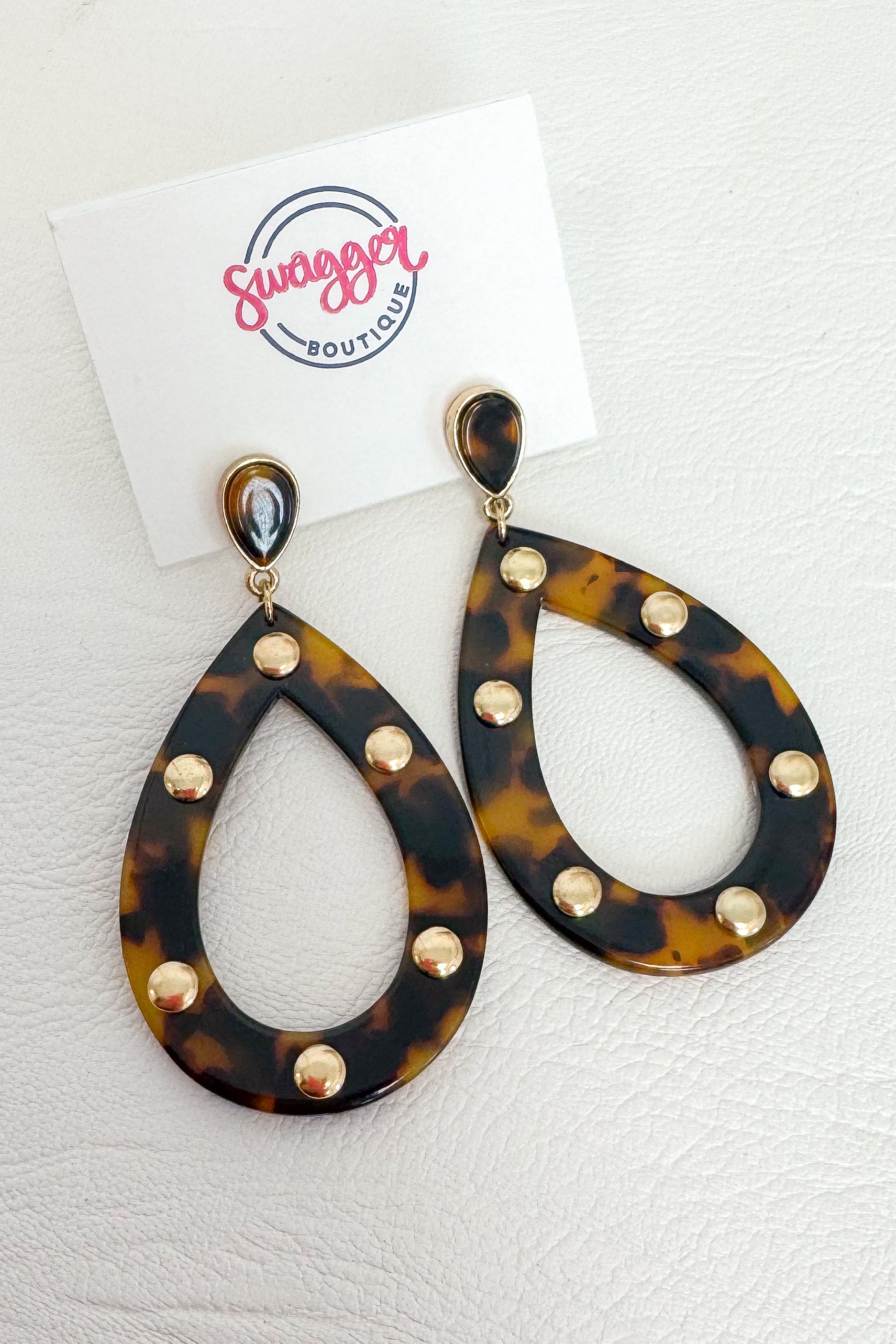 Tortoiseshell teardrop dangle earrings with gold-tone studs, displayed on a white card labeled Swagger Boutique against a white textured background.