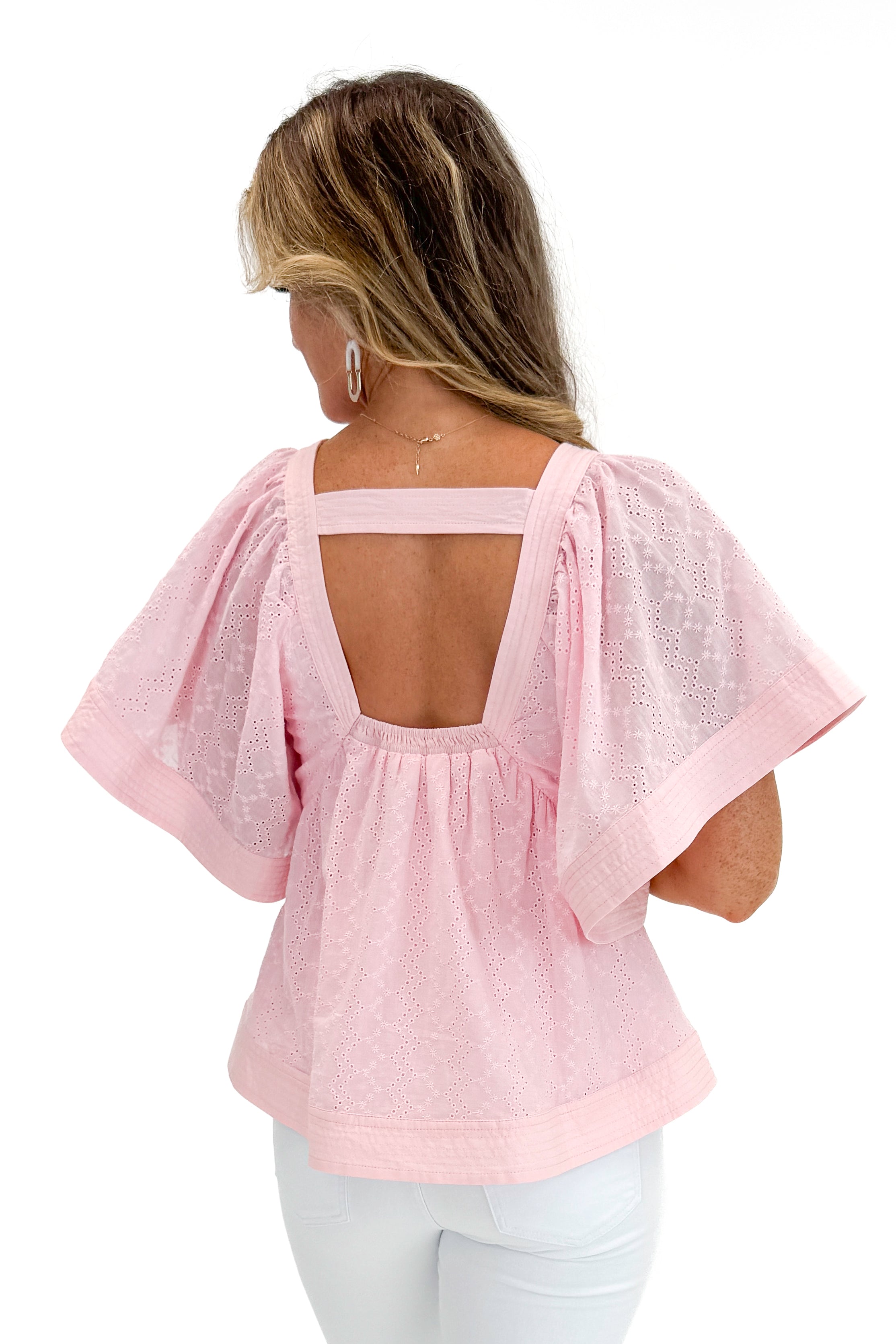 Back view of woman wearing Swagger Boutiqueβs Pink Eyelet V-Neck Top with jeans against white studio background.