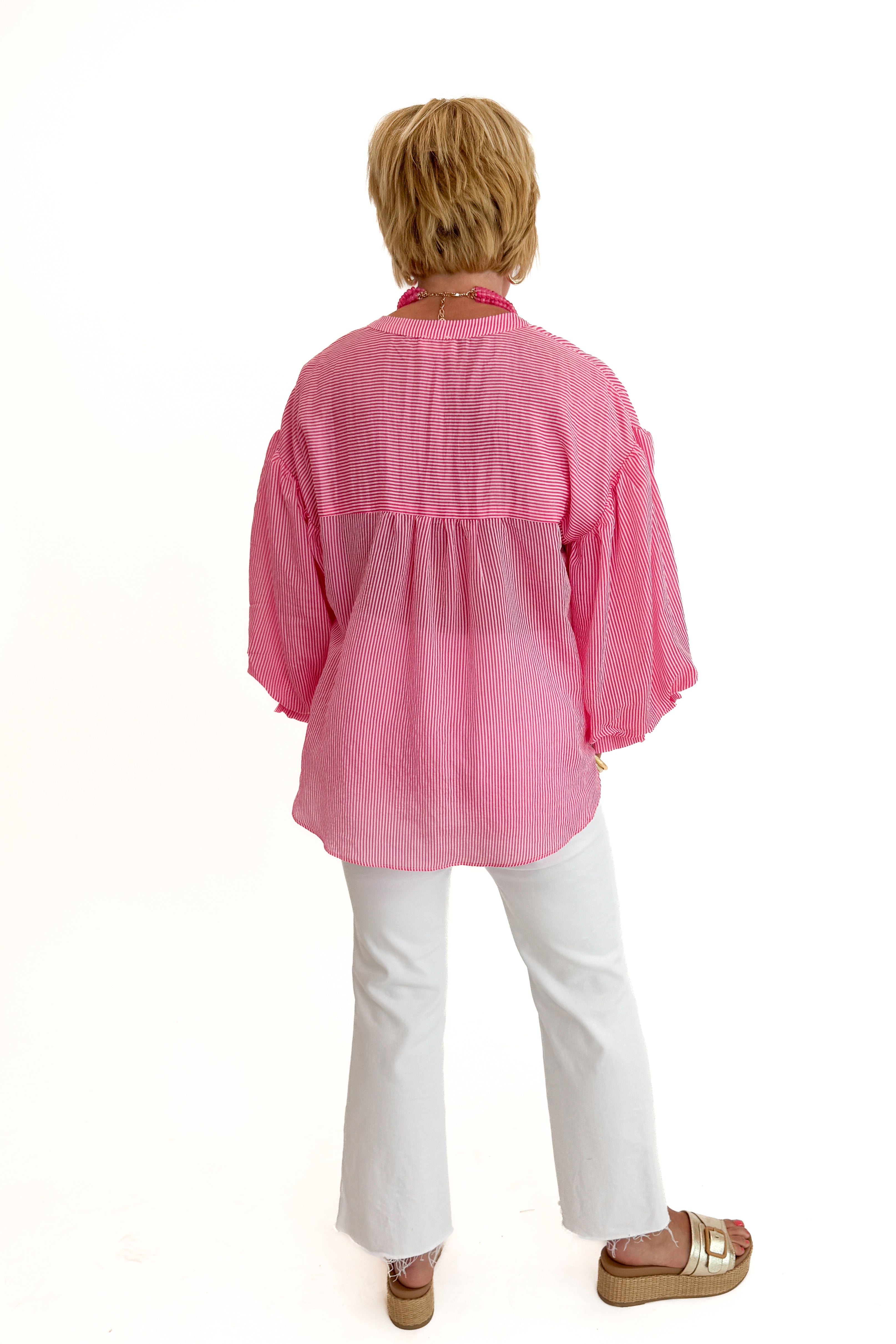 Back view of woman wearing Swagger Boutiqueβs Pink Pinstripe Bubble Sleeve Top with jeans against white studio background.
