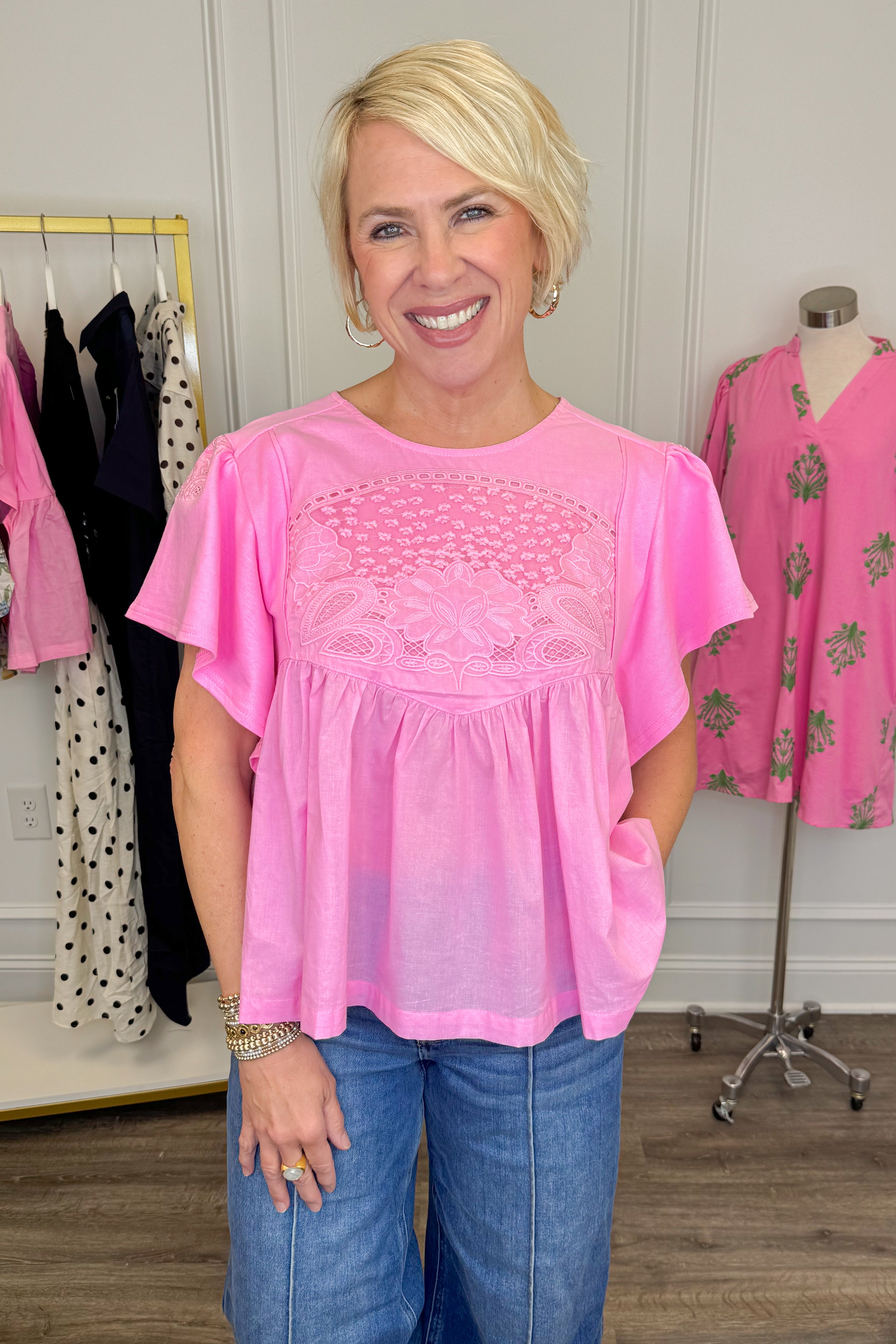 Front view of woman wearing Swagger Boutiqueโs Pink Embroidered Peplum Top with jeans with clothes around her.