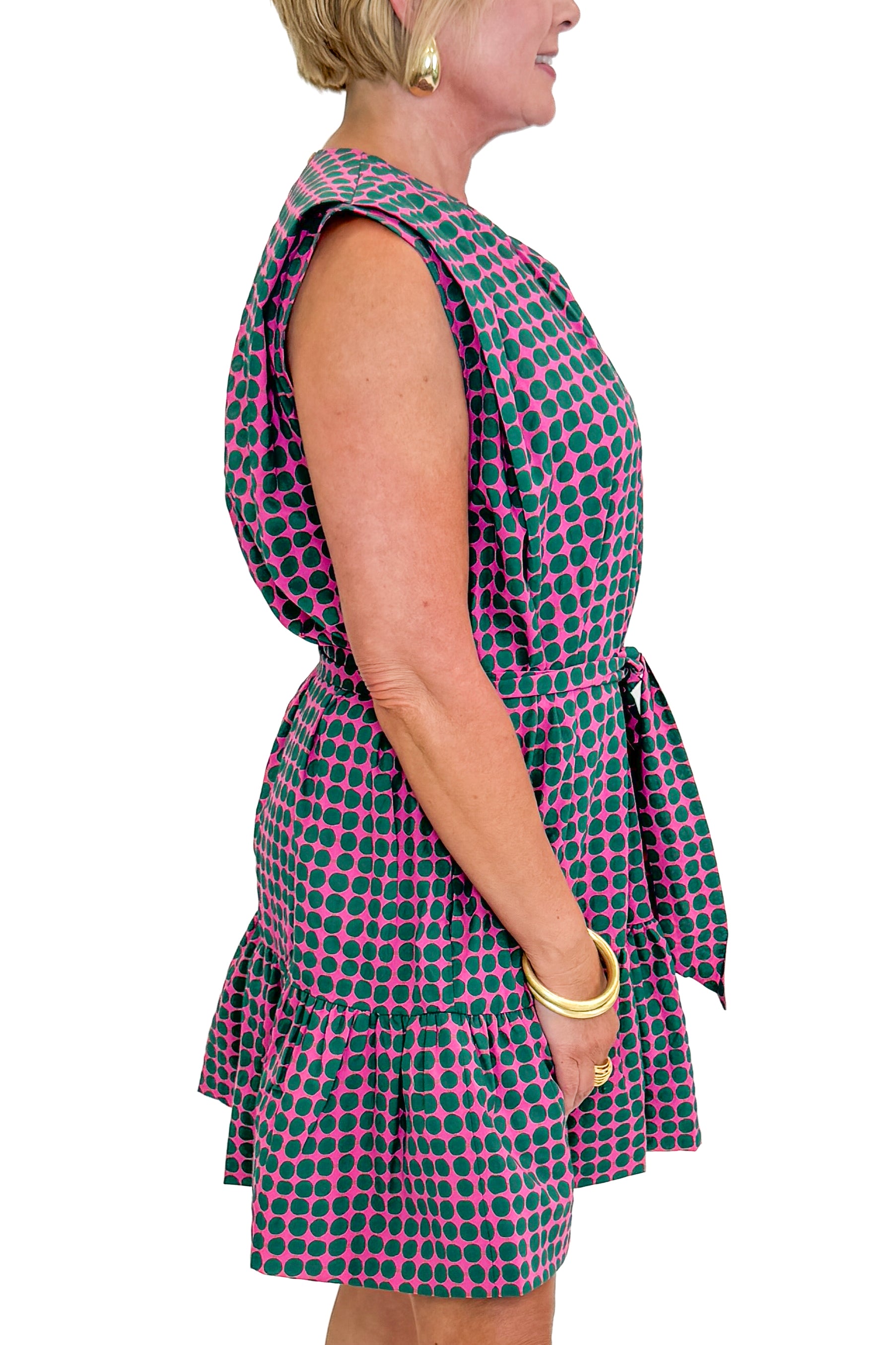 Side detail view of woman wearing Swagger Boutiqueβs Pink & Green Polka Dot Mini Dress with sandals against white studio background.