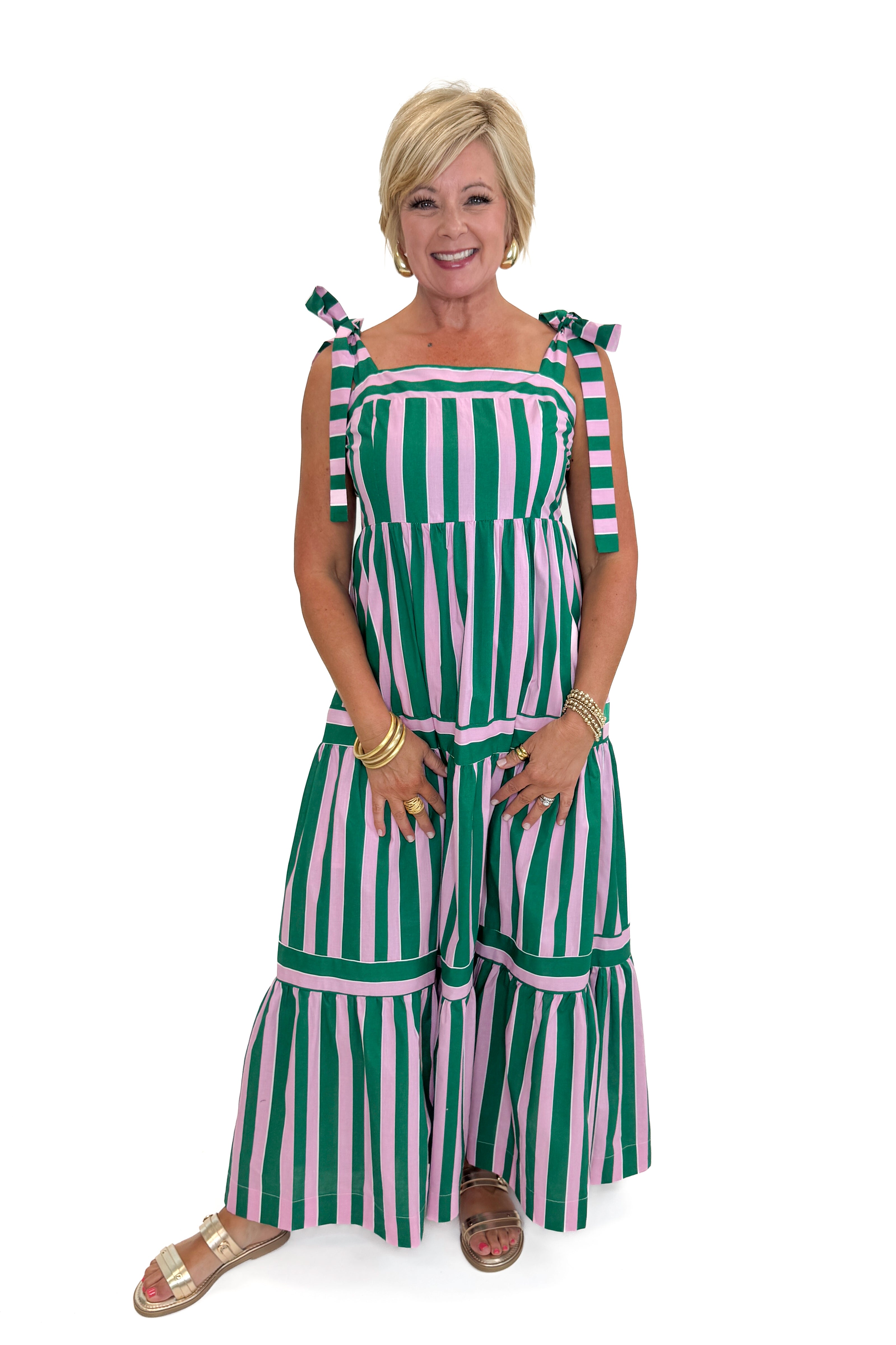 Front view of woman wearing Swagger Boutiqueβs Pink & Green Striped Tiered Maxi Dress with sandals against white studio background.