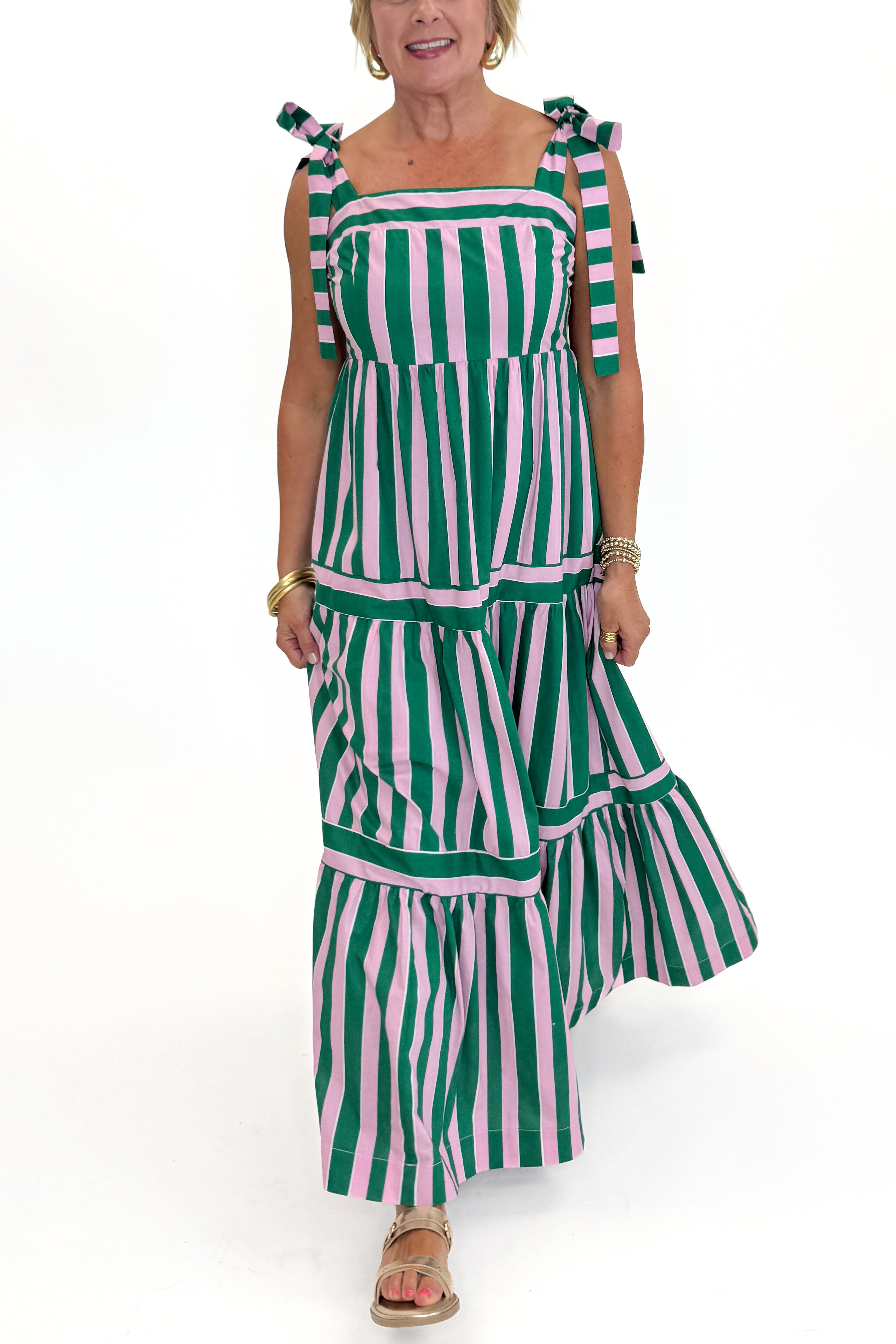Front detail view of woman wearing Swagger Boutiqueβs Pink & Green Striped Tiered Maxi Dress with sandals against white studio background.