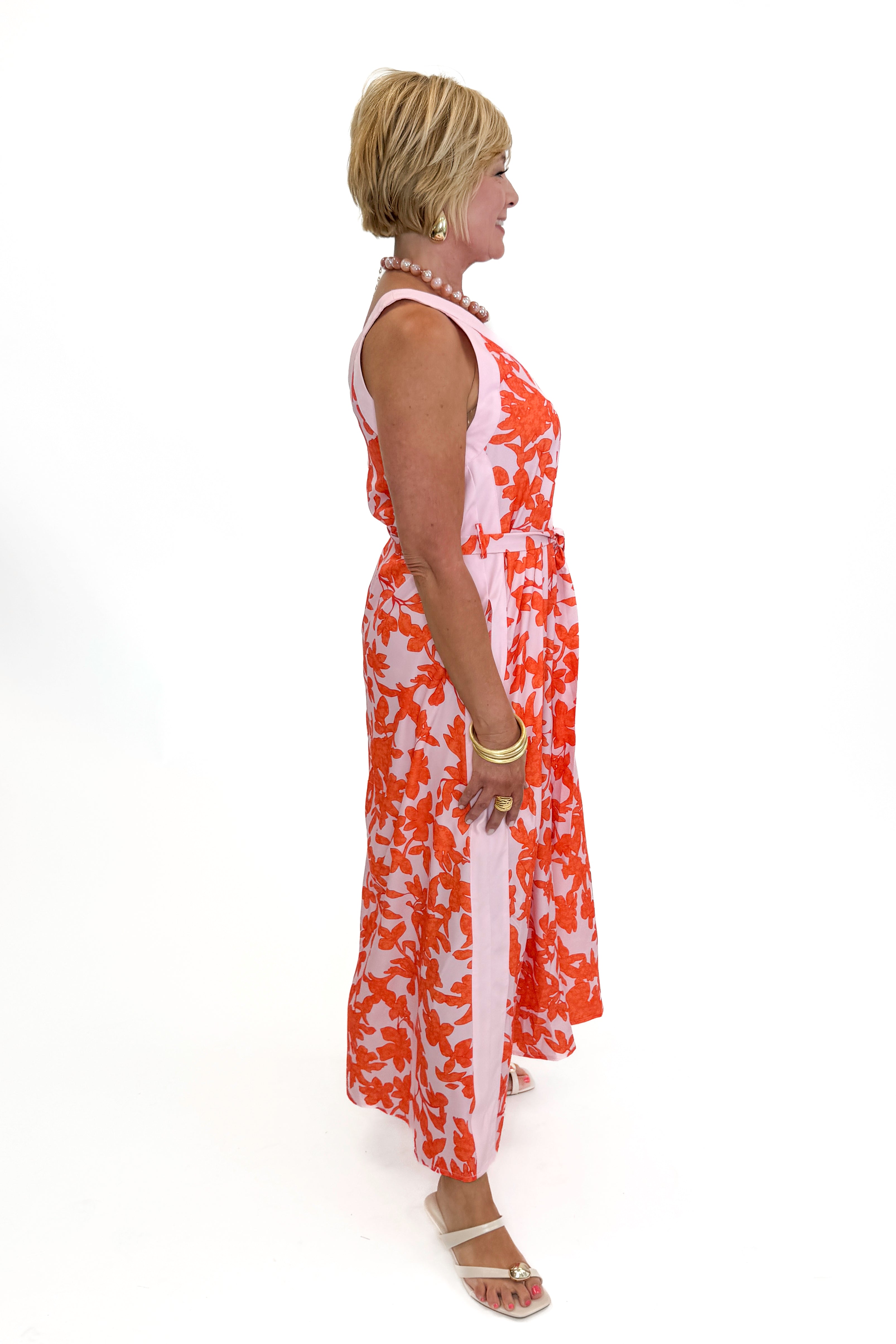 Side view of woman wearing Swagger Boutiqueβs Pink & Orange Floral Midi Dress by Entro with heels against white studio background.