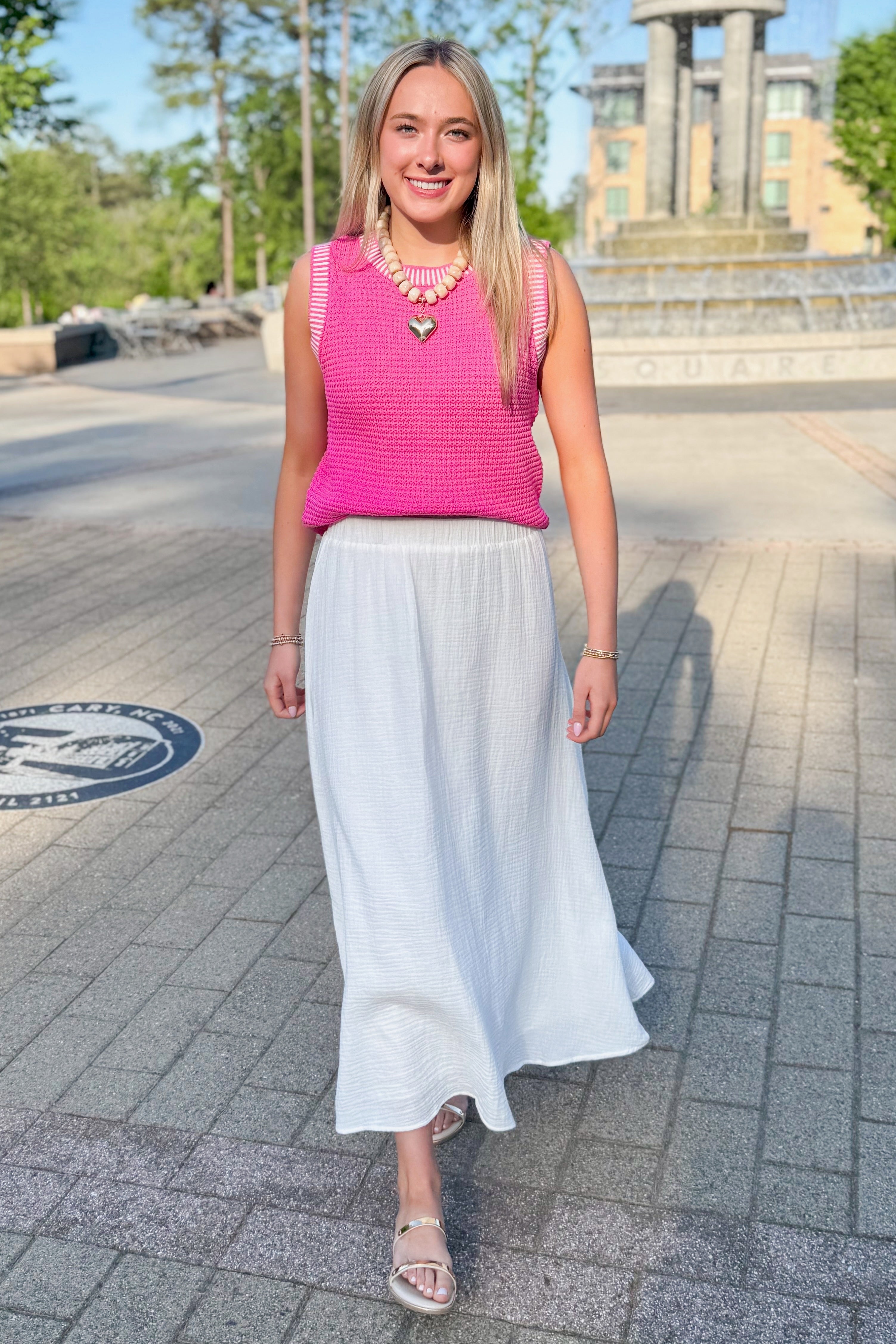 Front view of woman wearing Above All Else Pink & White Textured Sweater Tank with white skirt walking outside.