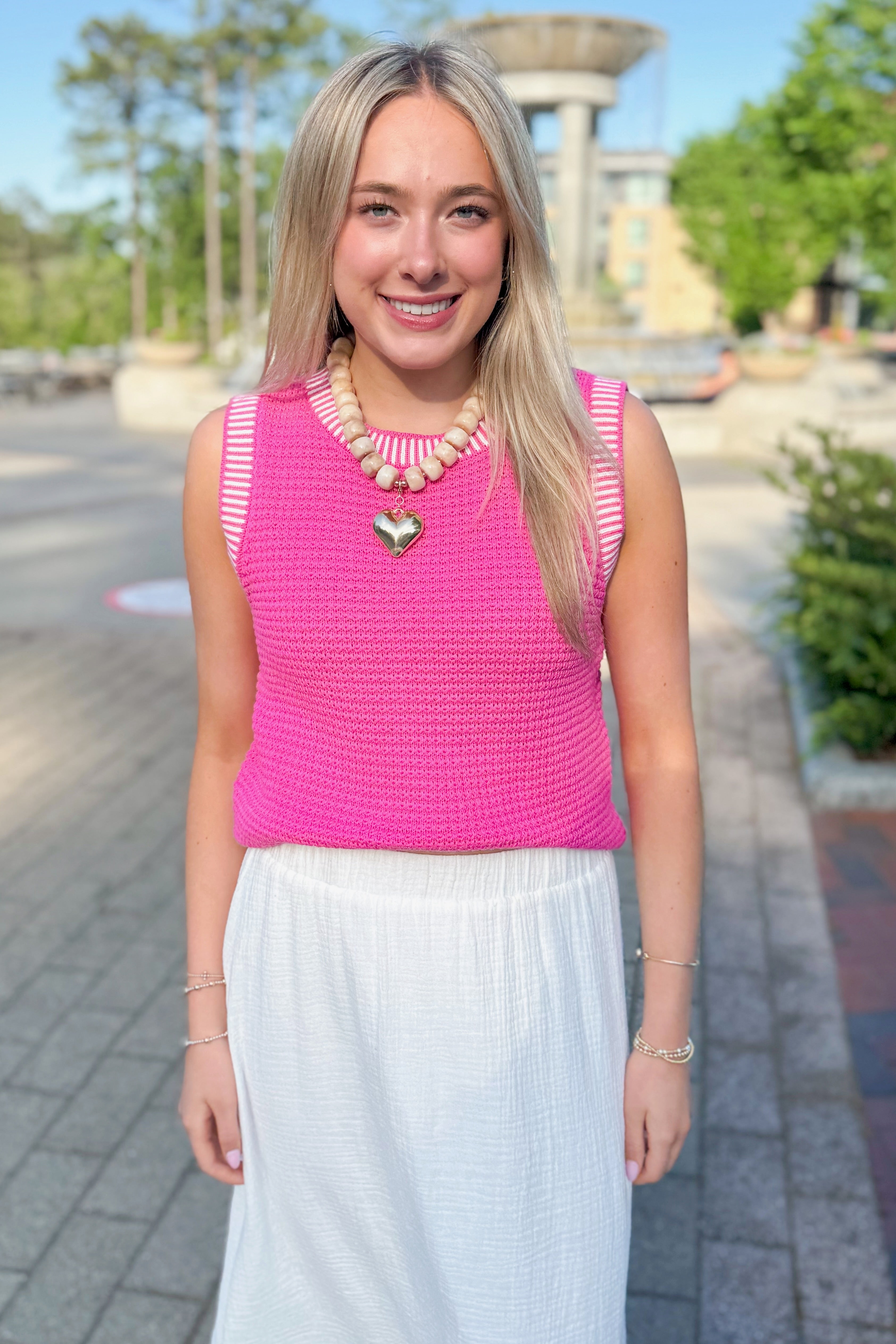 Front view of woman wearing Above All Else Pink & White Textured Sweater Tank with white skirt walking outside.