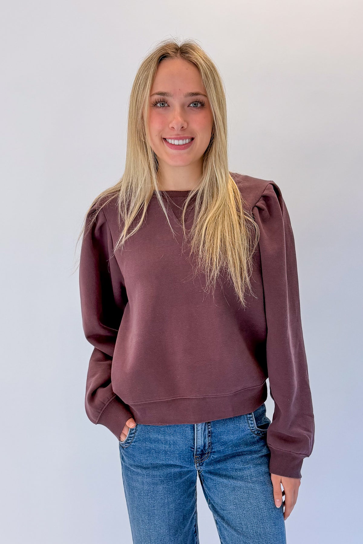 Front view of woman wearing Swagger Boutique’s Plum Puff Sleeve Sweatshirt with jeans against white studio background.