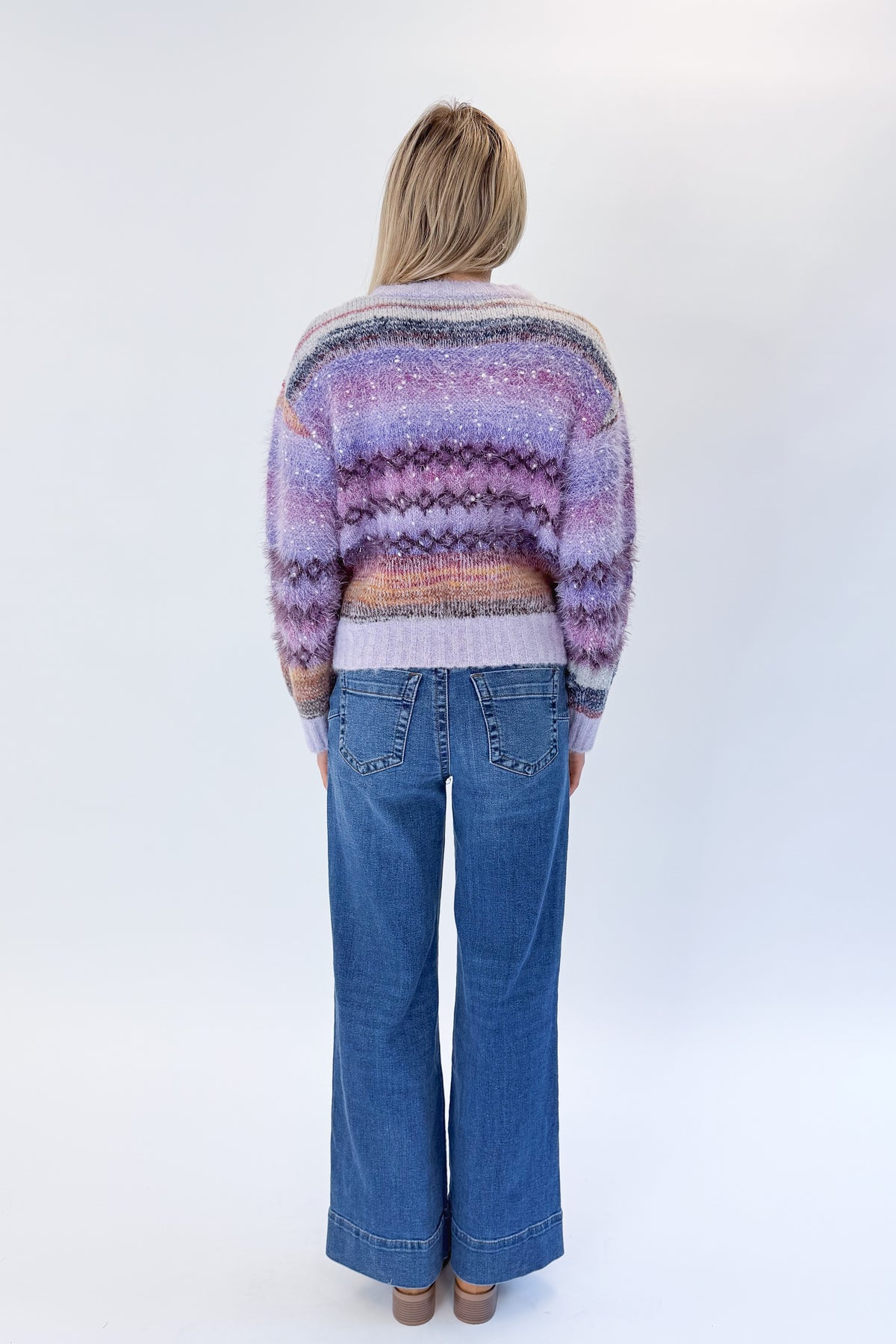 Back view of woman wearing Swagger Boutique’s Purple Printed Eyelash Sweater with jeans against white studio background.