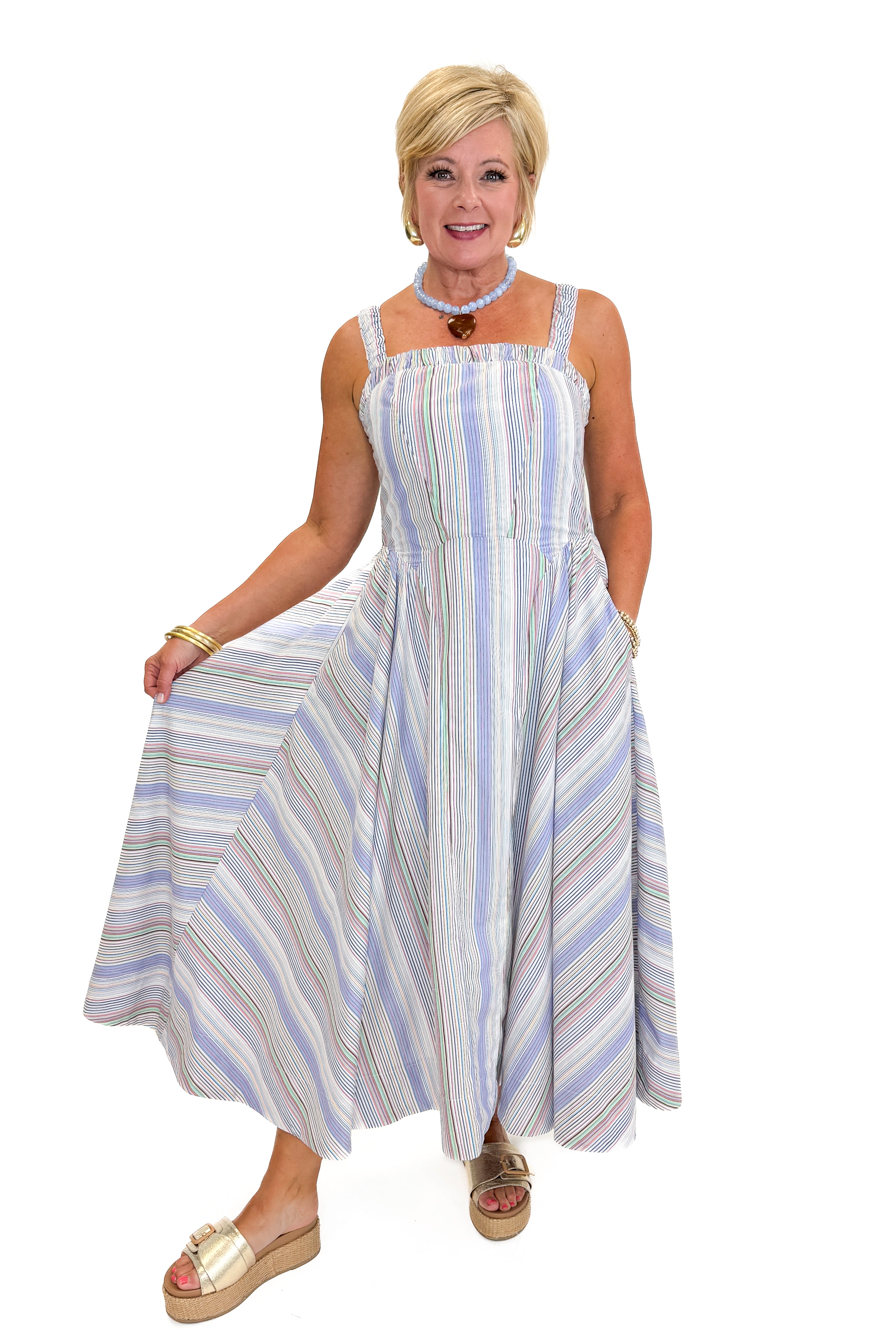 Front view of woman wearing Swagger Boutique’s Purple & Multi Striped Sleeveless Midi Dress with sandals against white studio background.