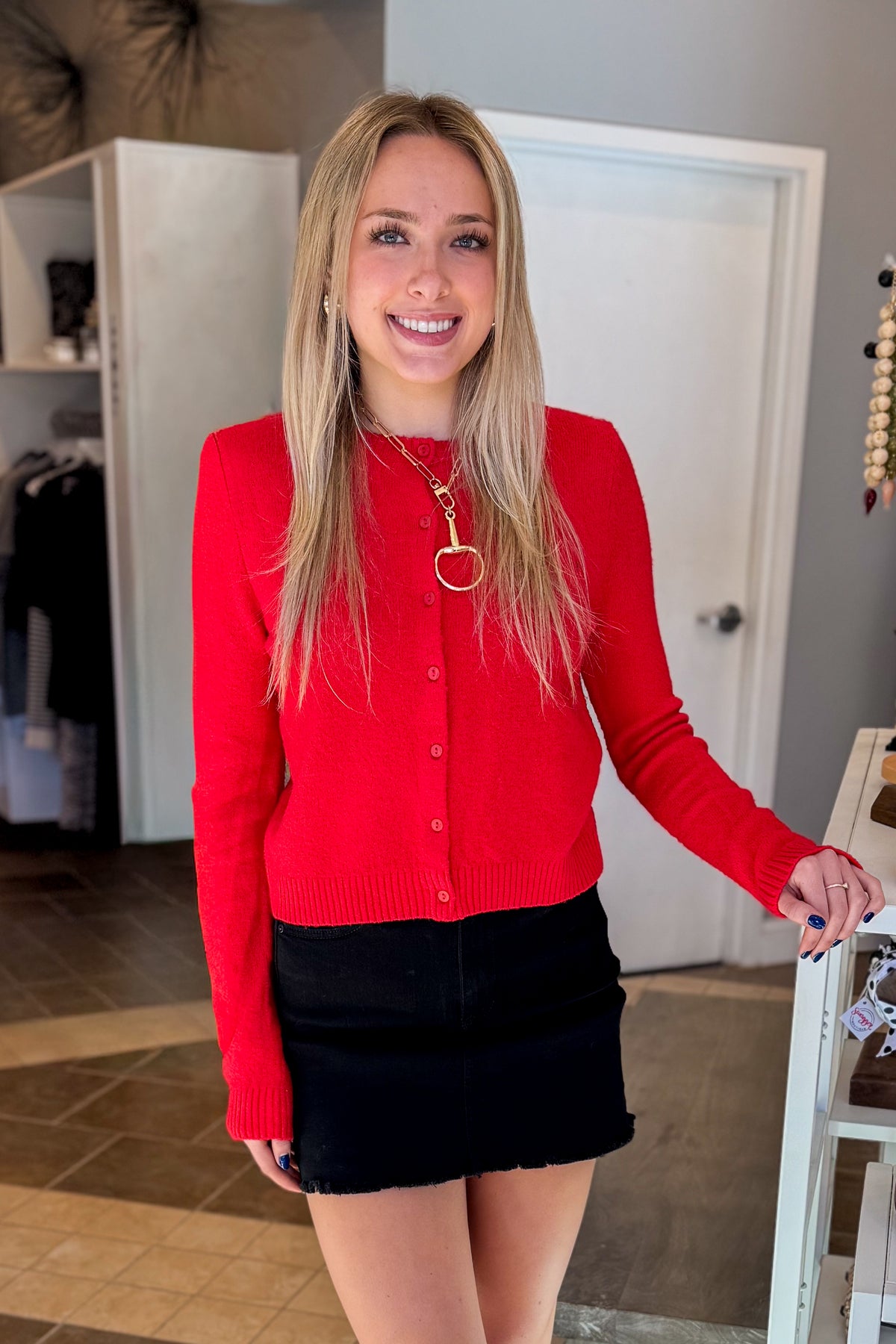 Front view of woman wearing Swagger Boutique’s Red Button Up Cardigan with Black Denim Mini Skirt by Just Black Denim standing at the store.