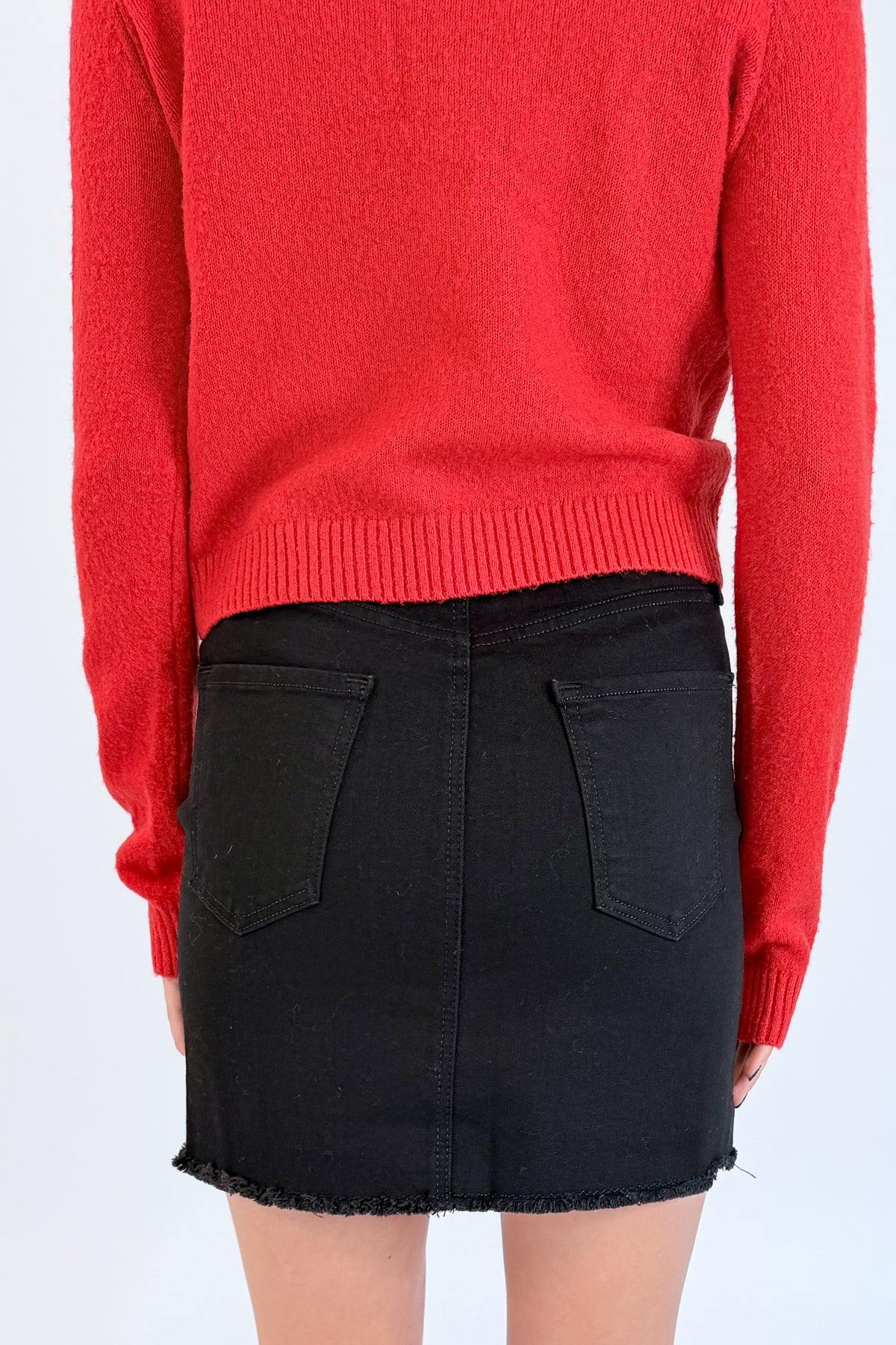 Back detail view of woman wearing Swagger Boutique’s Red Button Up Cardigan with Black Denim Mini Skirt by Just Black Denim against white studio background.