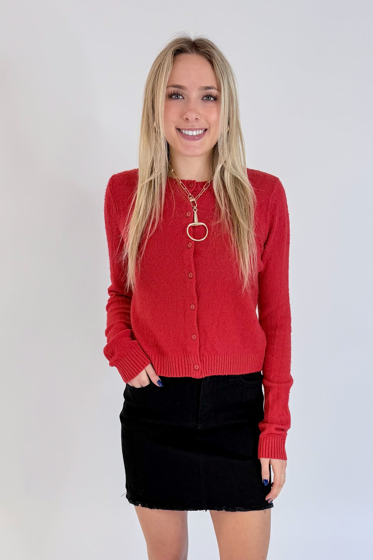 Front view of woman wearing Swagger Boutique’s Red Button Up Cardigan with Black Denim Mini Skirt by Just Black Denim against white studio background.