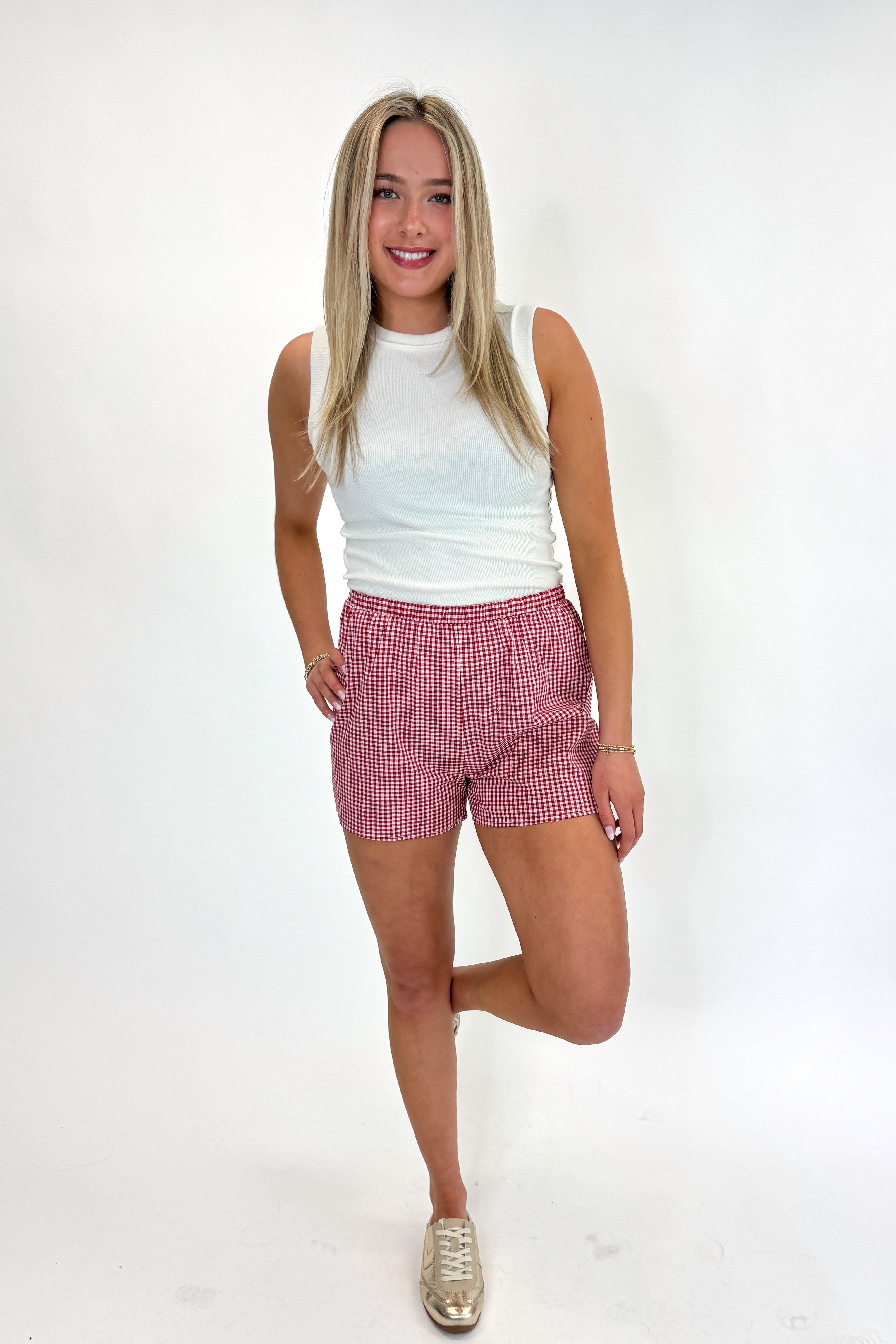 Front view of woman wearing Swagger Boutique’s Red Gingham Shorts with Off White Round Hem Ribbed Tank against white studio background.