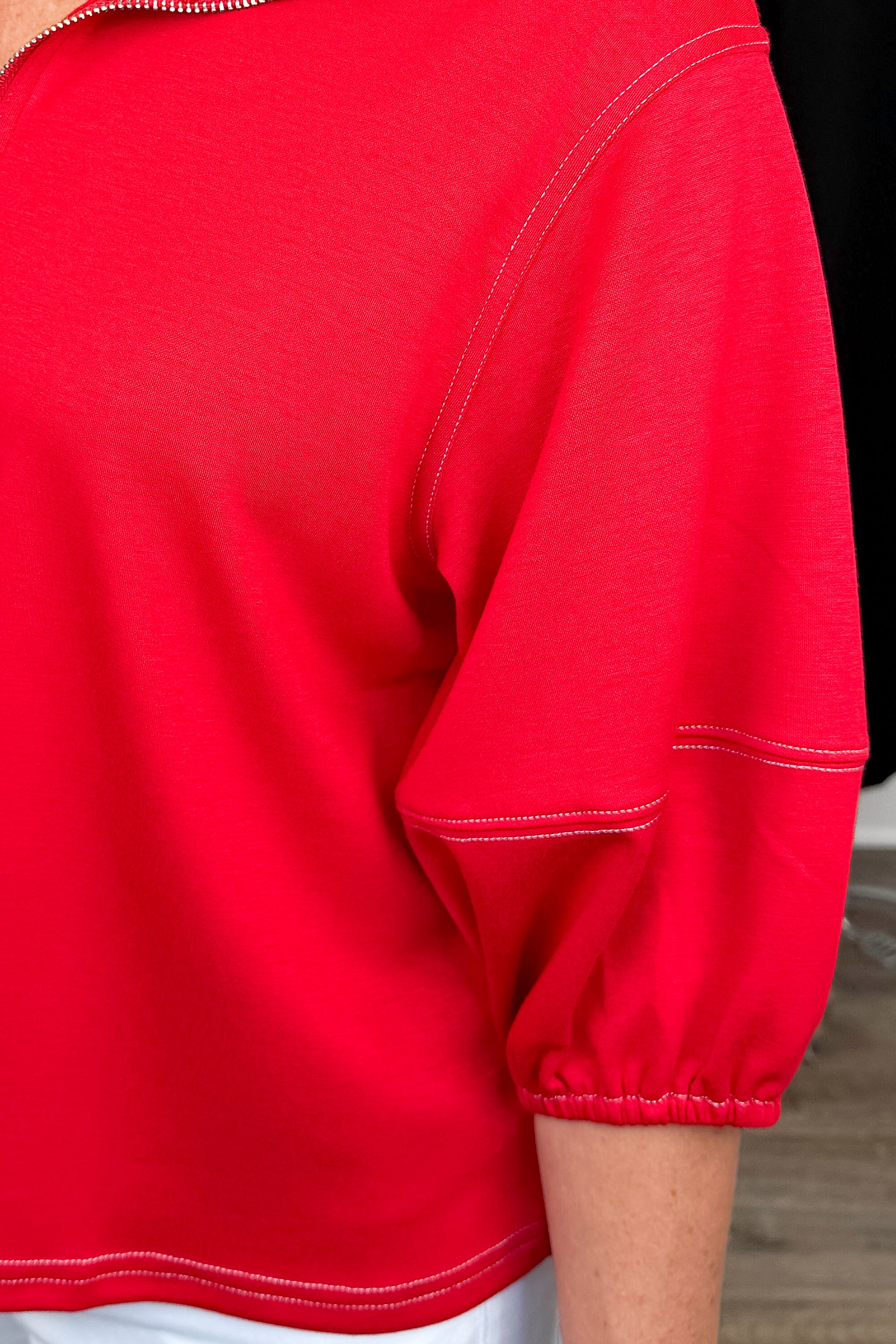 Front detail view of woman wearing Swagger Boutique’s Red Puff Sleeve 1_4 Zip Sweatshirt with jeans with clothing hanging in the background.
