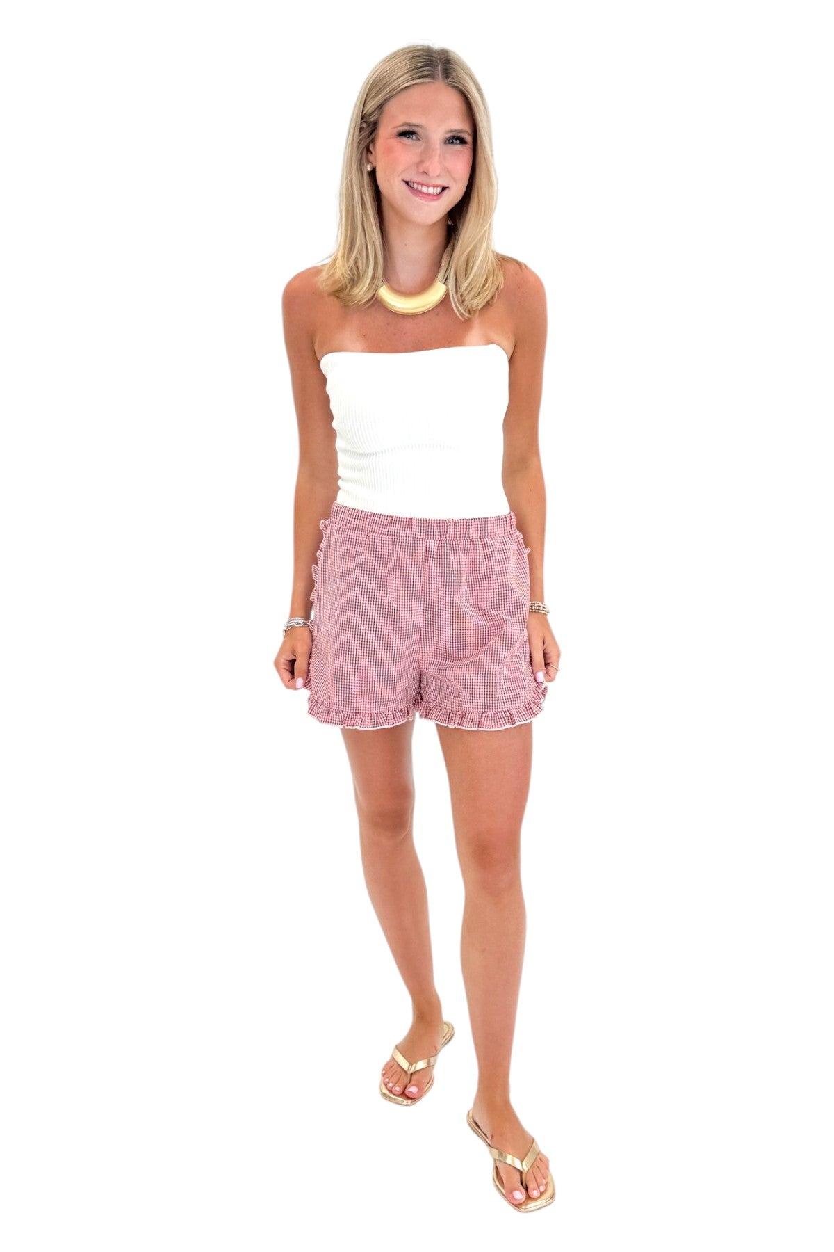 Front view of woman wearing Swagger Boutiqueās Red & White Gingham Ruffle Shorts with white top against white studio background.