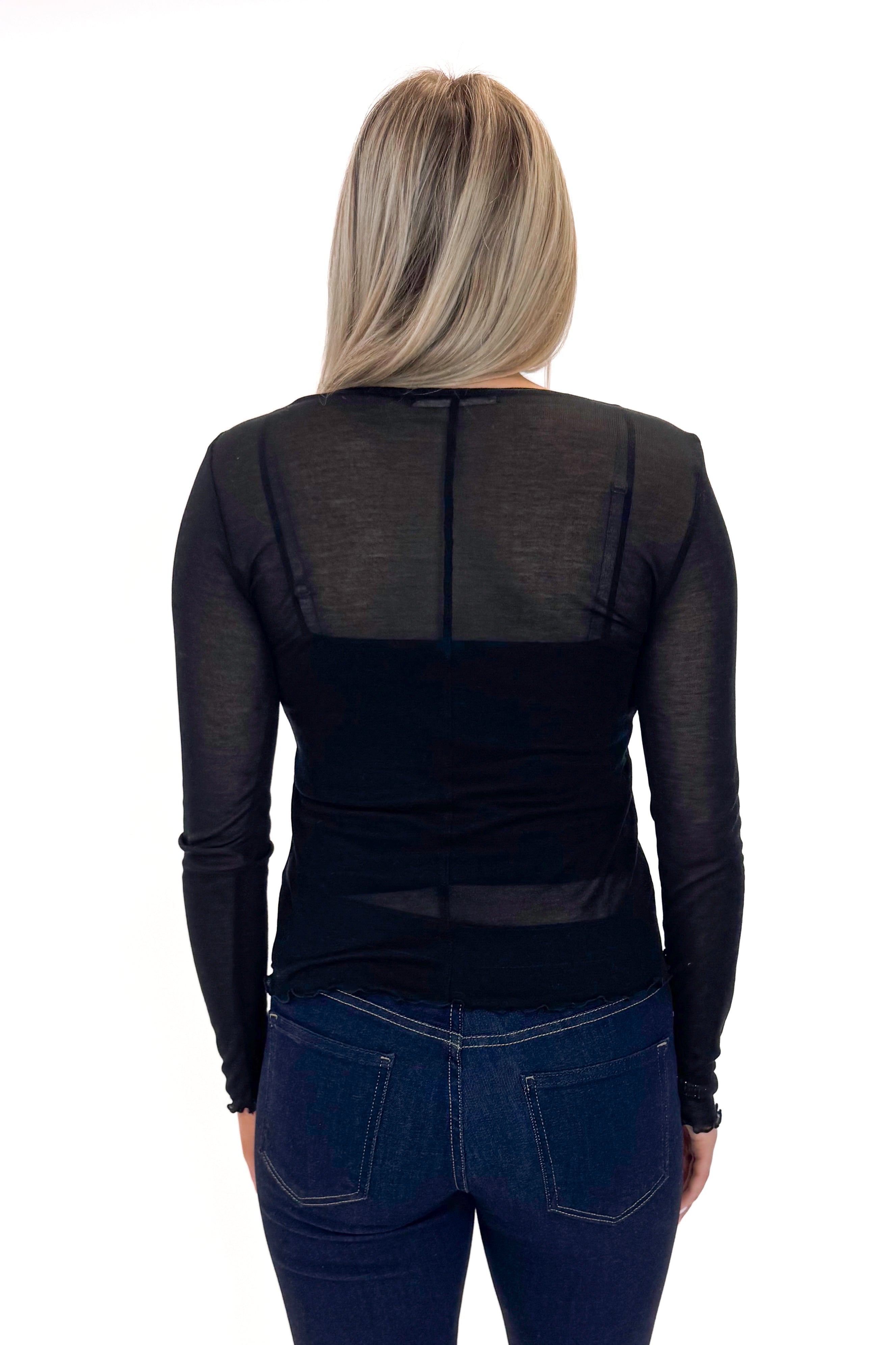 Back view of woman wearing Black Sheer Long Sleeve Top with jeans against white studio background.