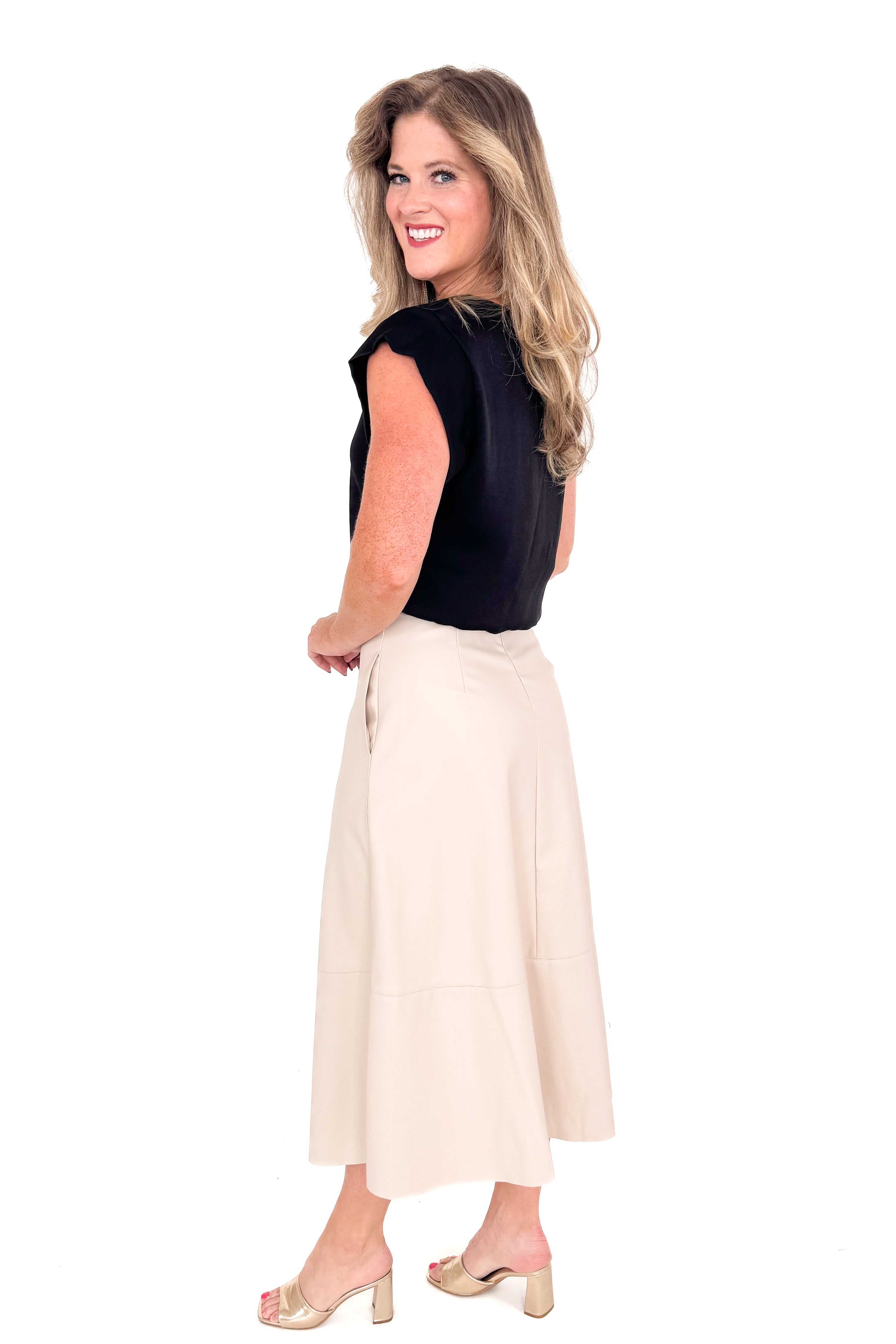 Side view of woman wearing black top with cream faux leather skirt against white studio background.