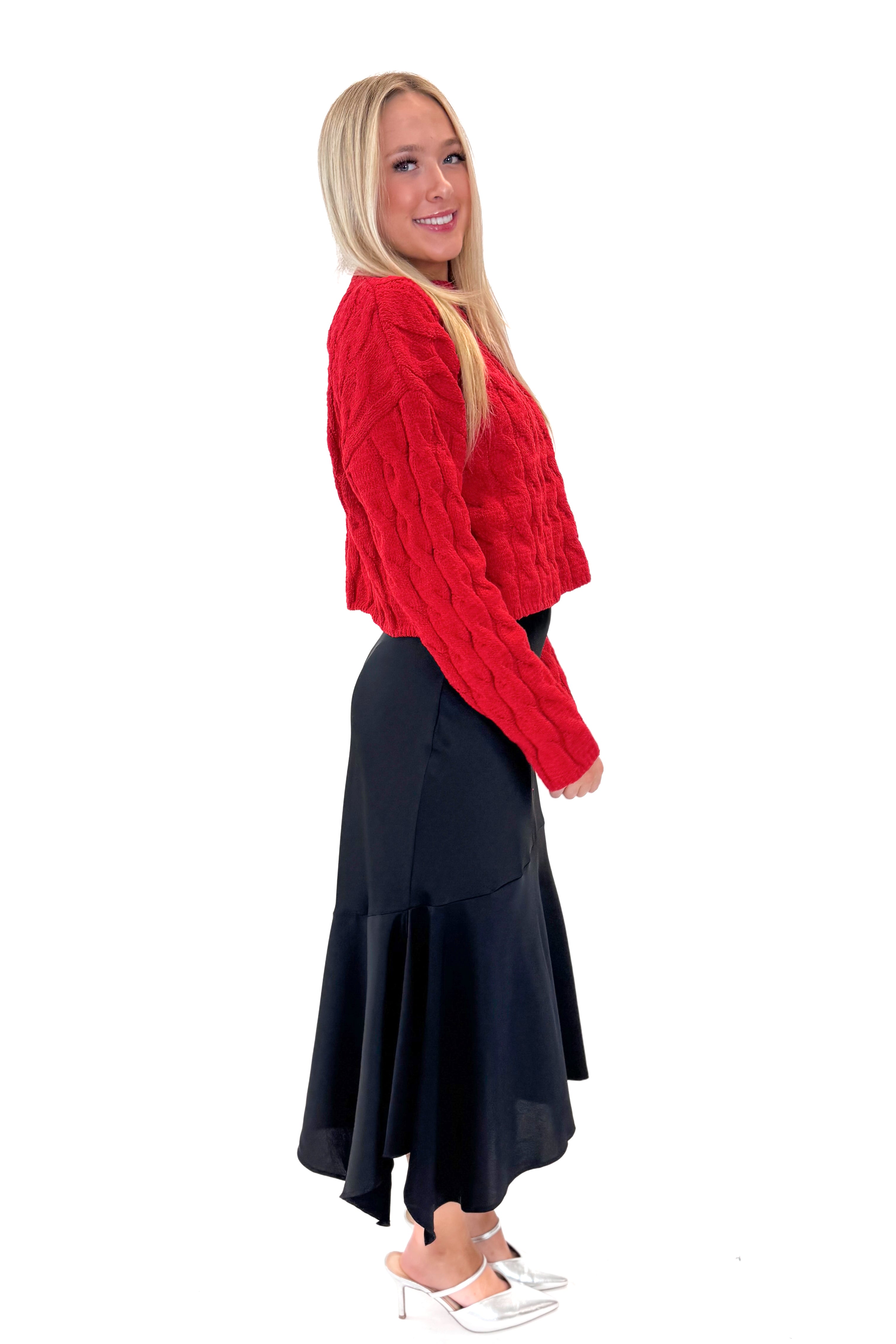 Side view of woman wearing Black Satin Handkerchief Hem Midi Skirt with sweater against white studio background.