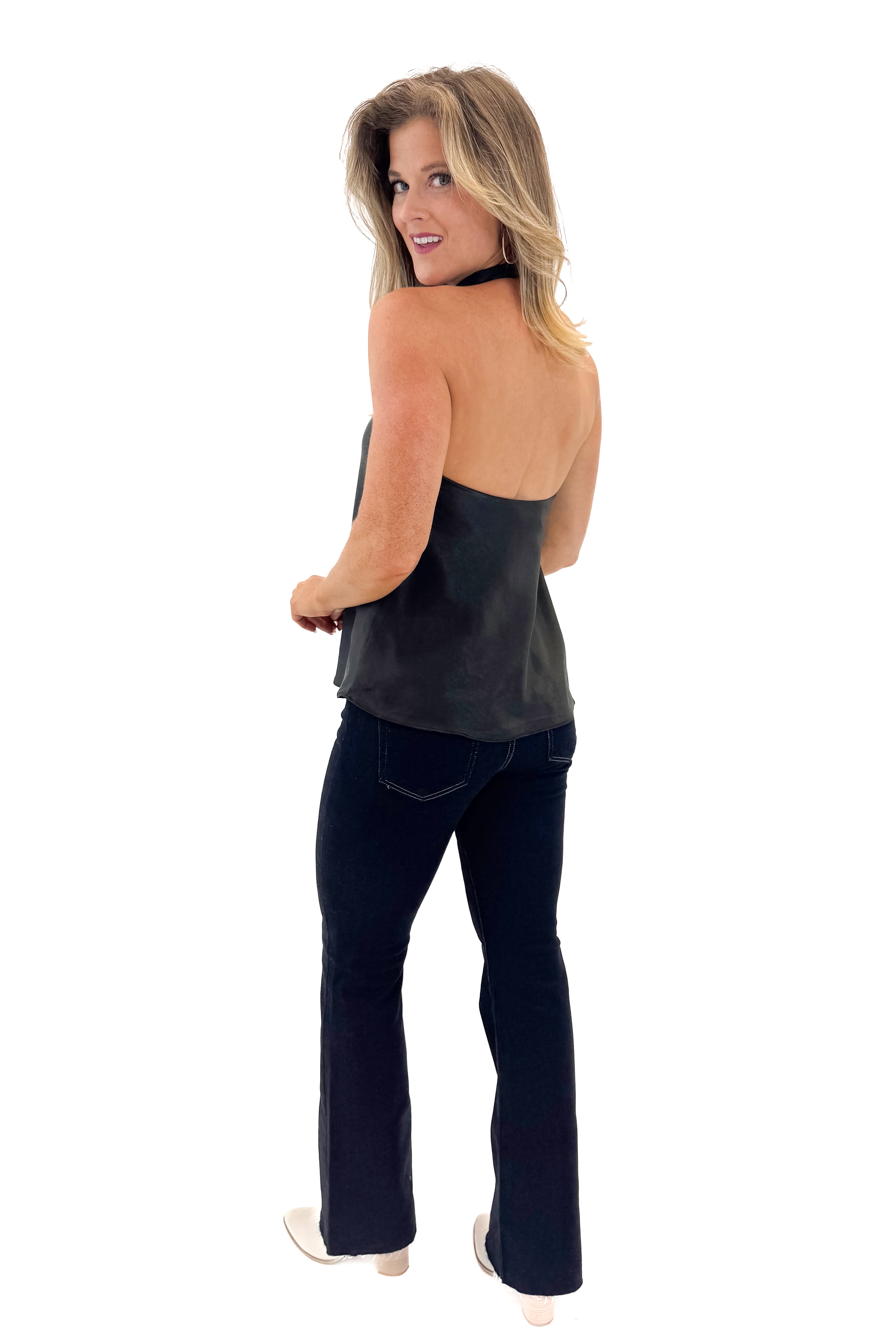 Side view of woman wearing Black Satin Halter Neck Top with jeans against white studio background.