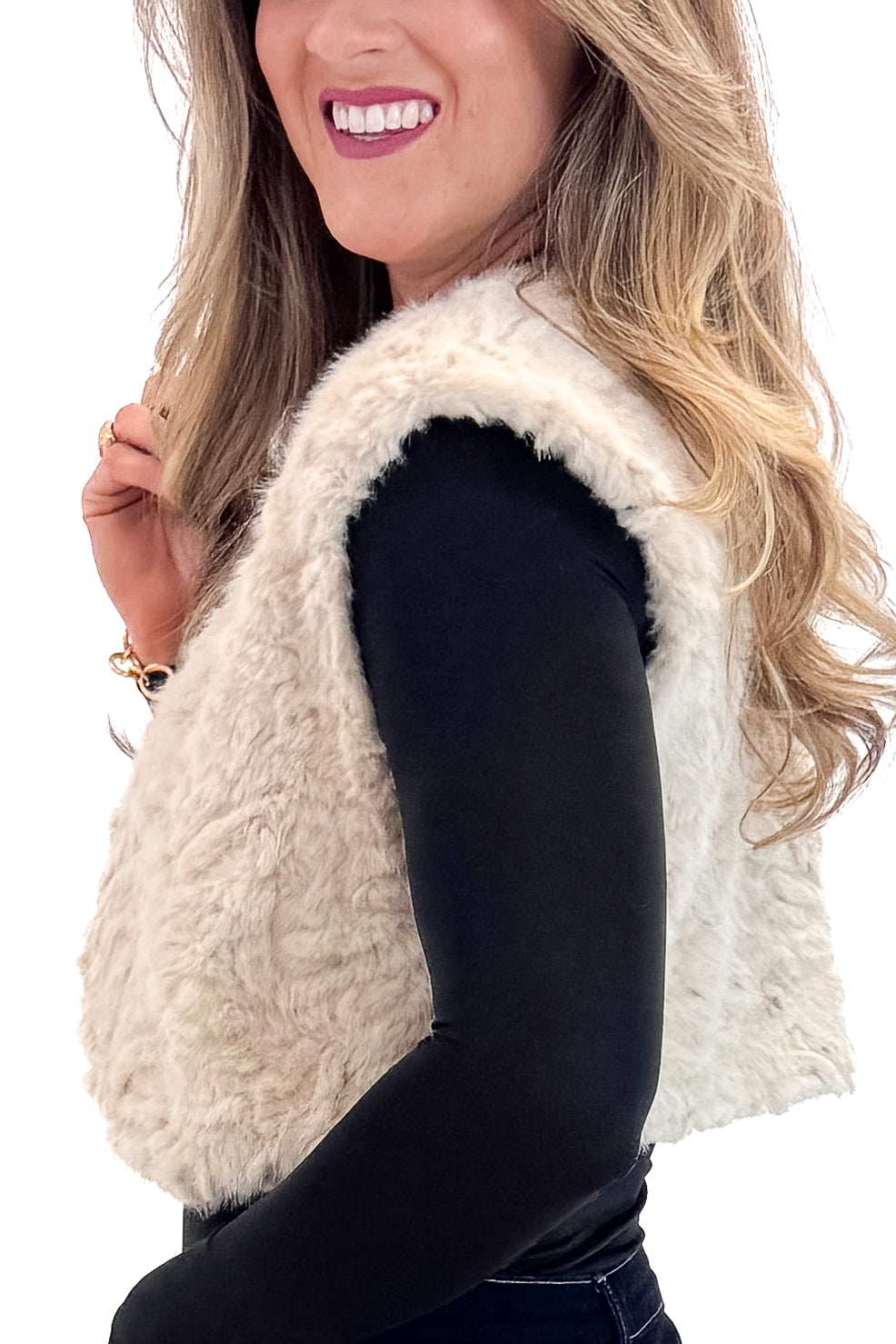 Side view of woman wearing Taupe Cropped Faux Fur Vest with jeans against white studio background.