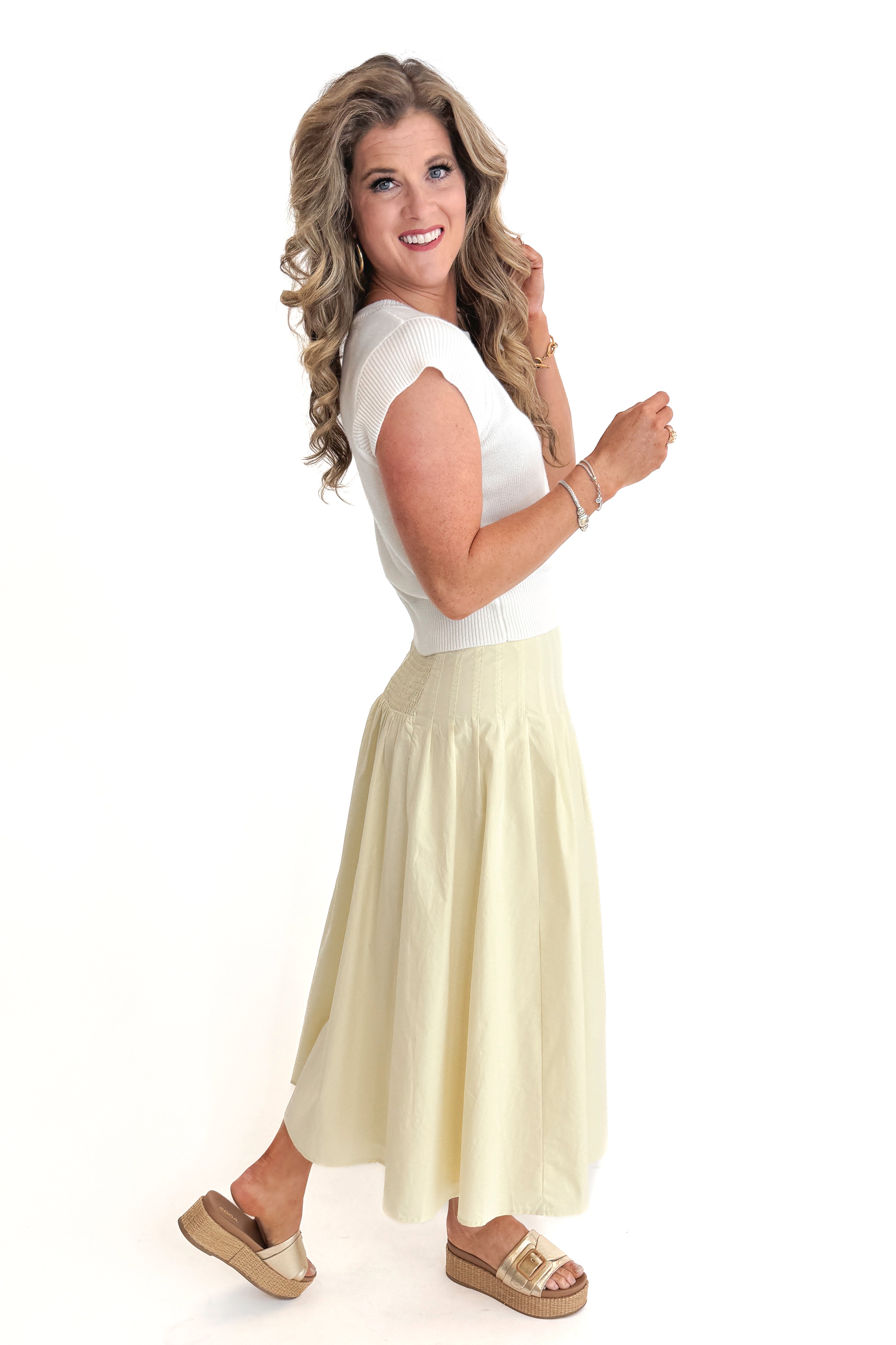 Side view of woman wearing top with Yellow Pleat Detail Midi Skirt against white studio background.