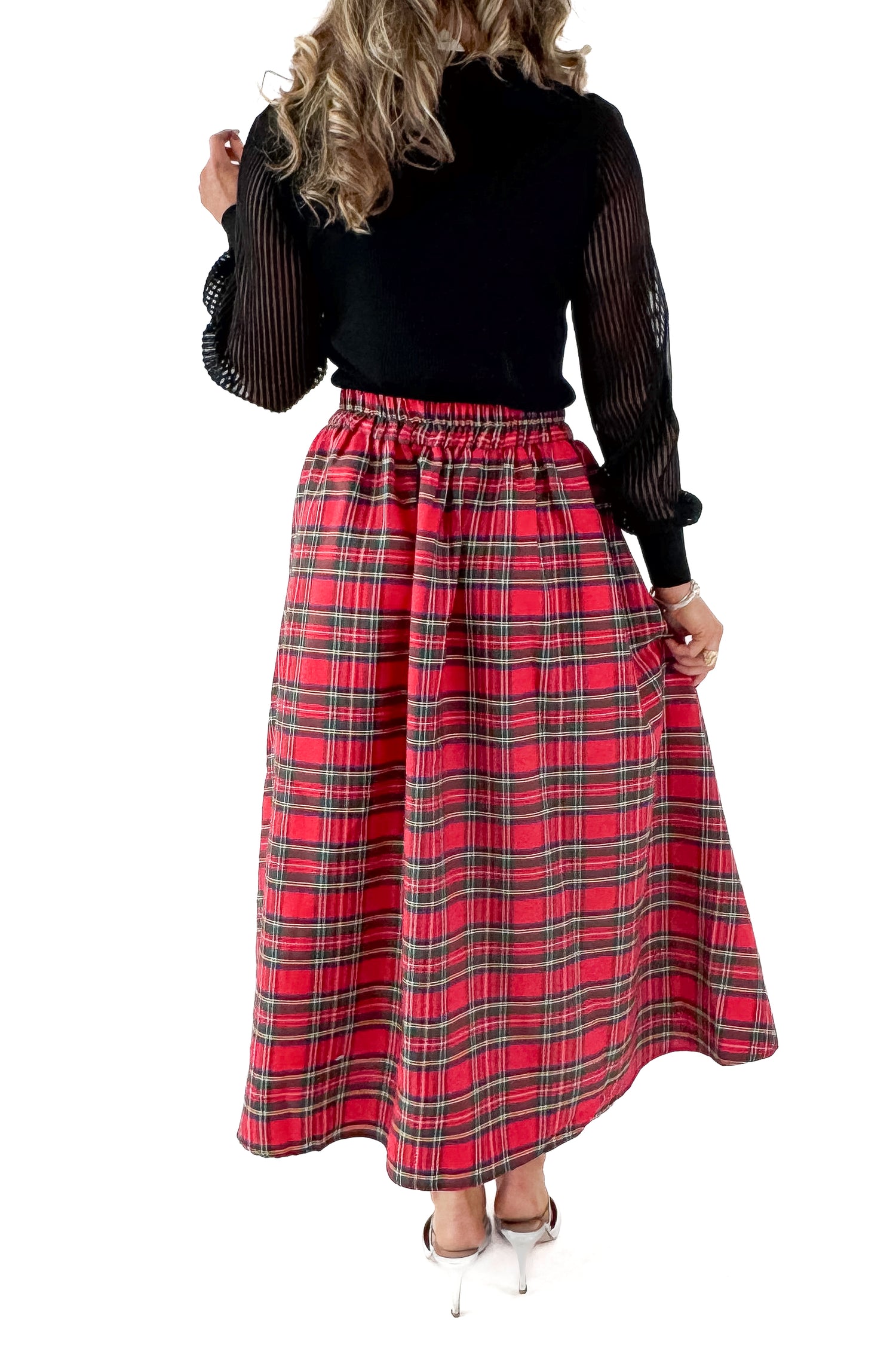 Back view of woman wearing black top with red tartan skirt against white studio background.