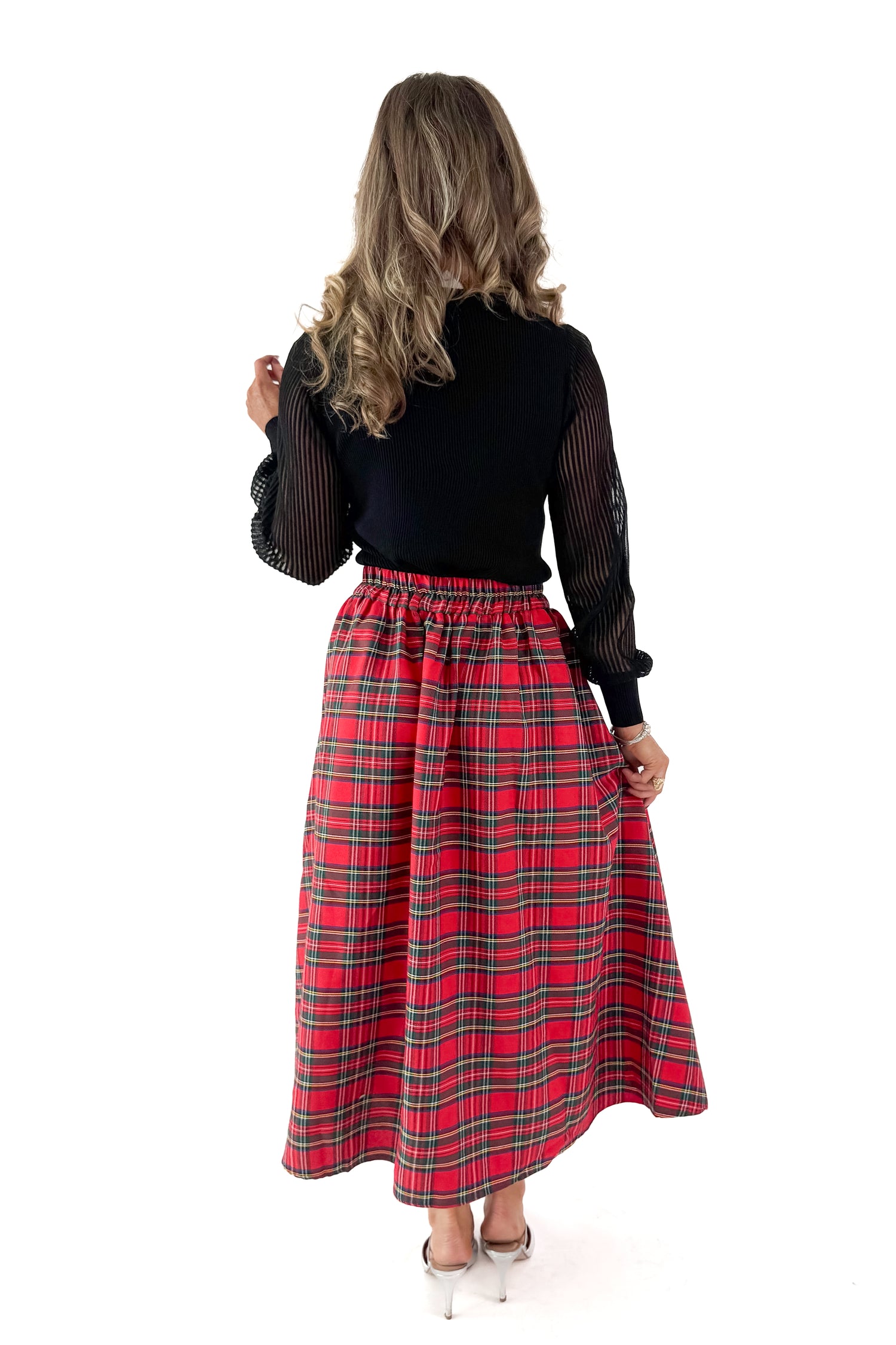 Back view of woman wearing black top with red tartan skirt against white studio background.