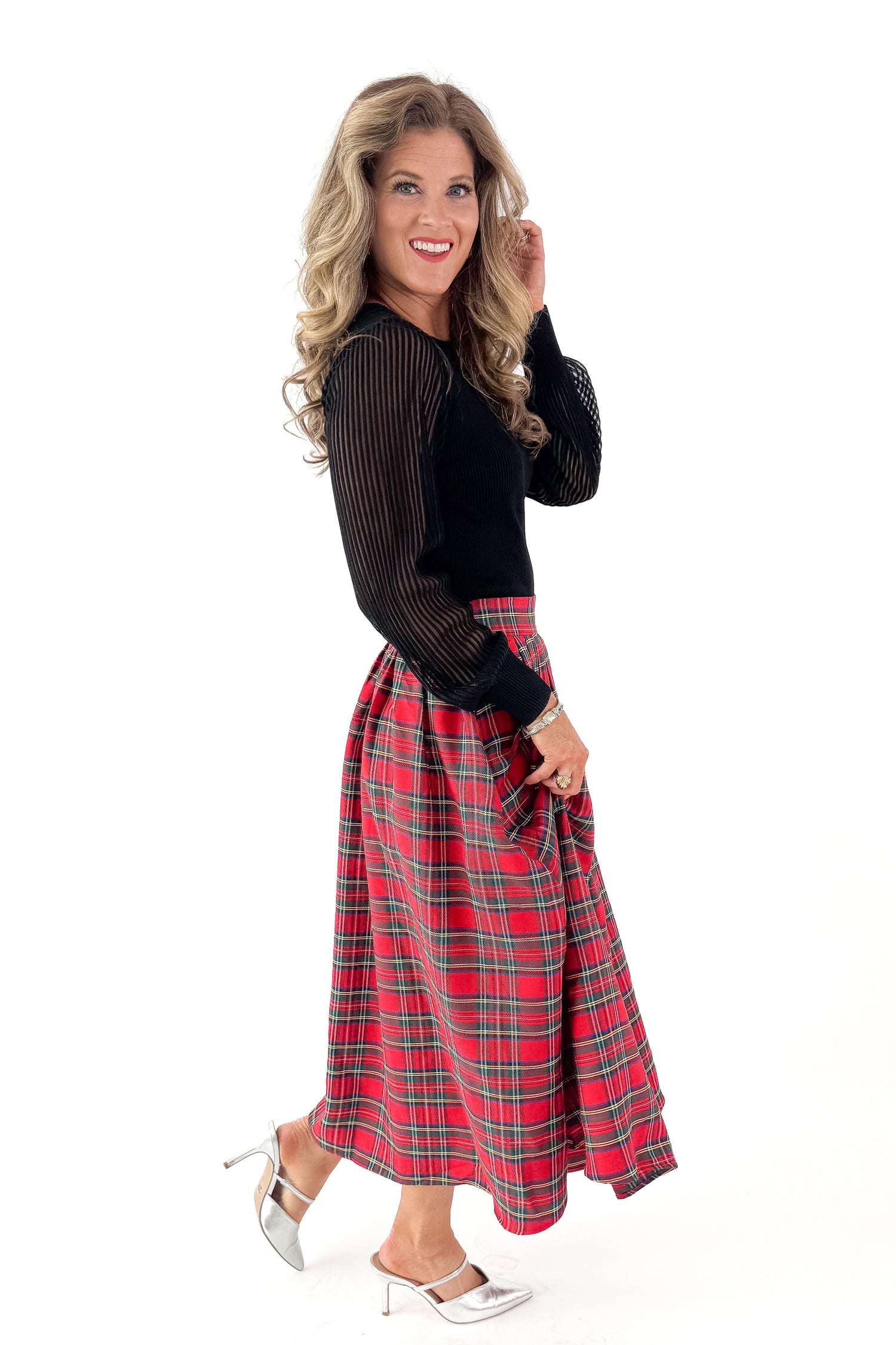 Side view of woman wearing black top with red tartan skirt against white studio background.