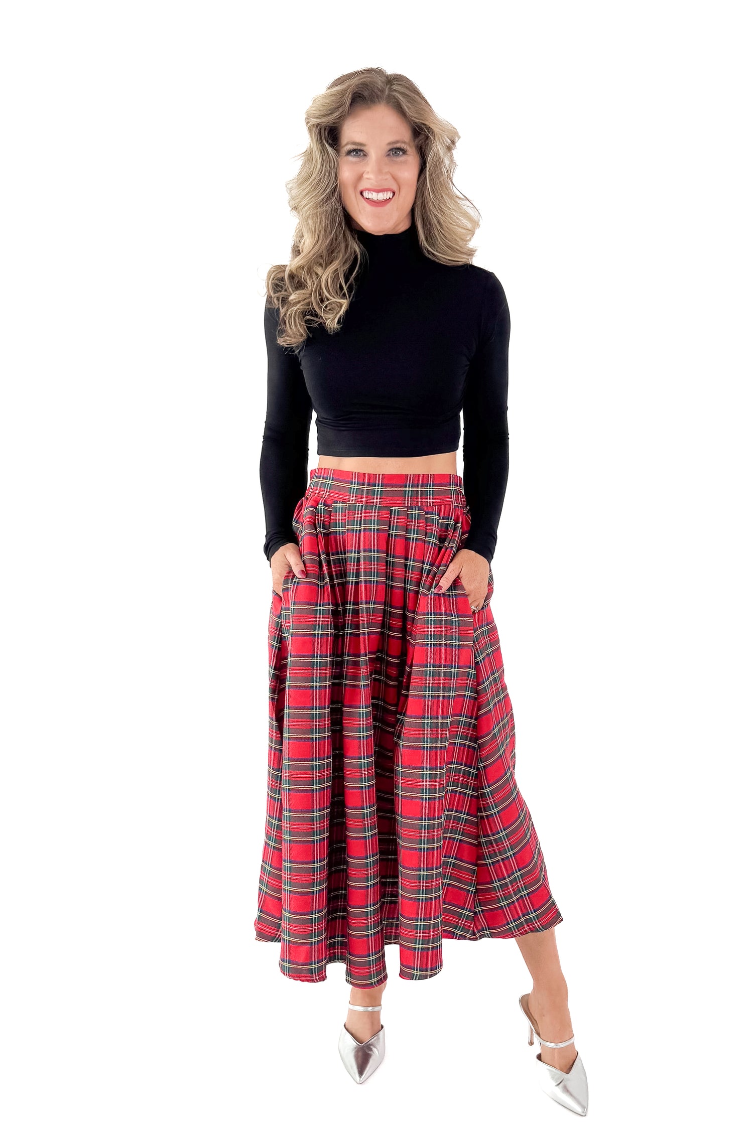 Front view of woman wearing black top with red tartan skirt against white studio background.