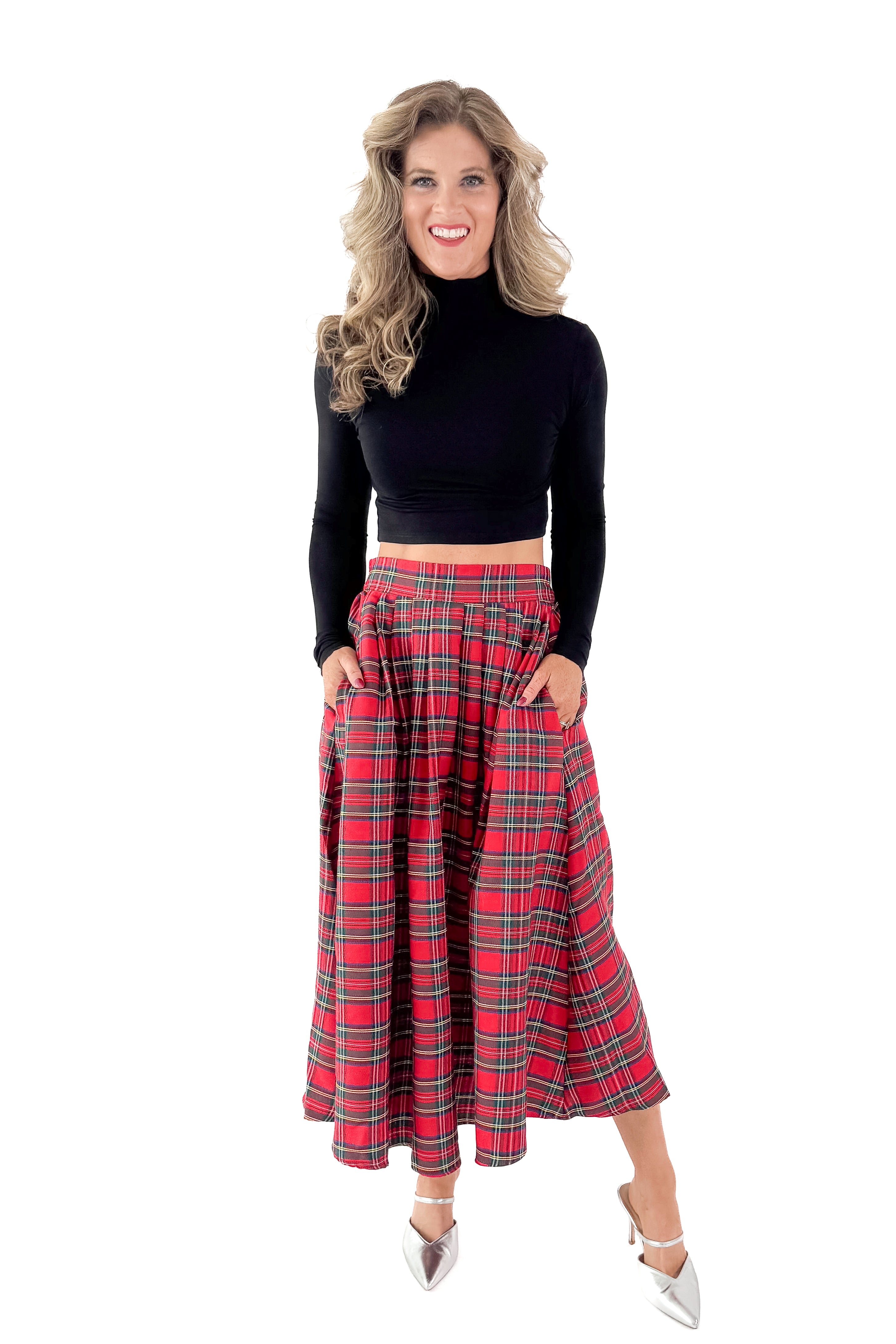 Front view of woman wearing black top with red tartan skirt against white studio background.