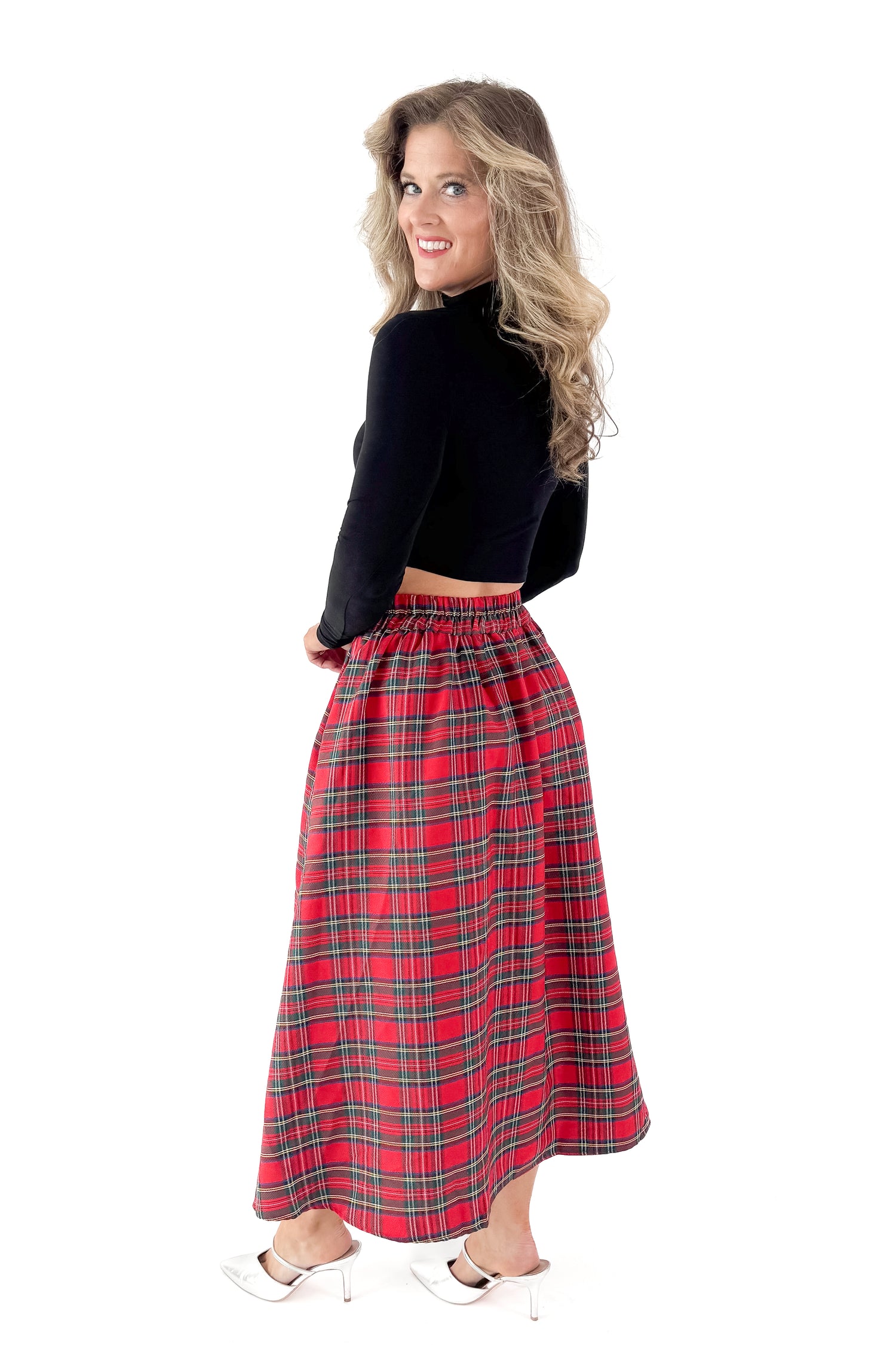 Side view of woman wearing black top with red tartan skirt against white studio background.