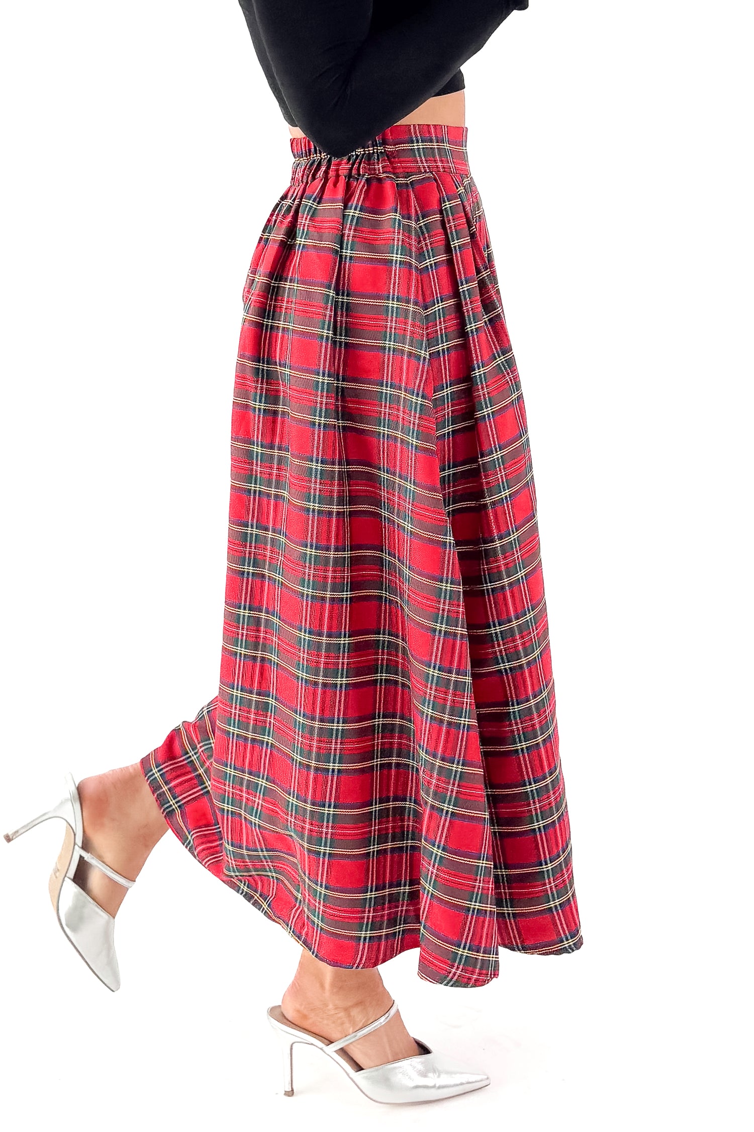 Side detailed view of woman wearing black top with red tartan skirt against white studio background.